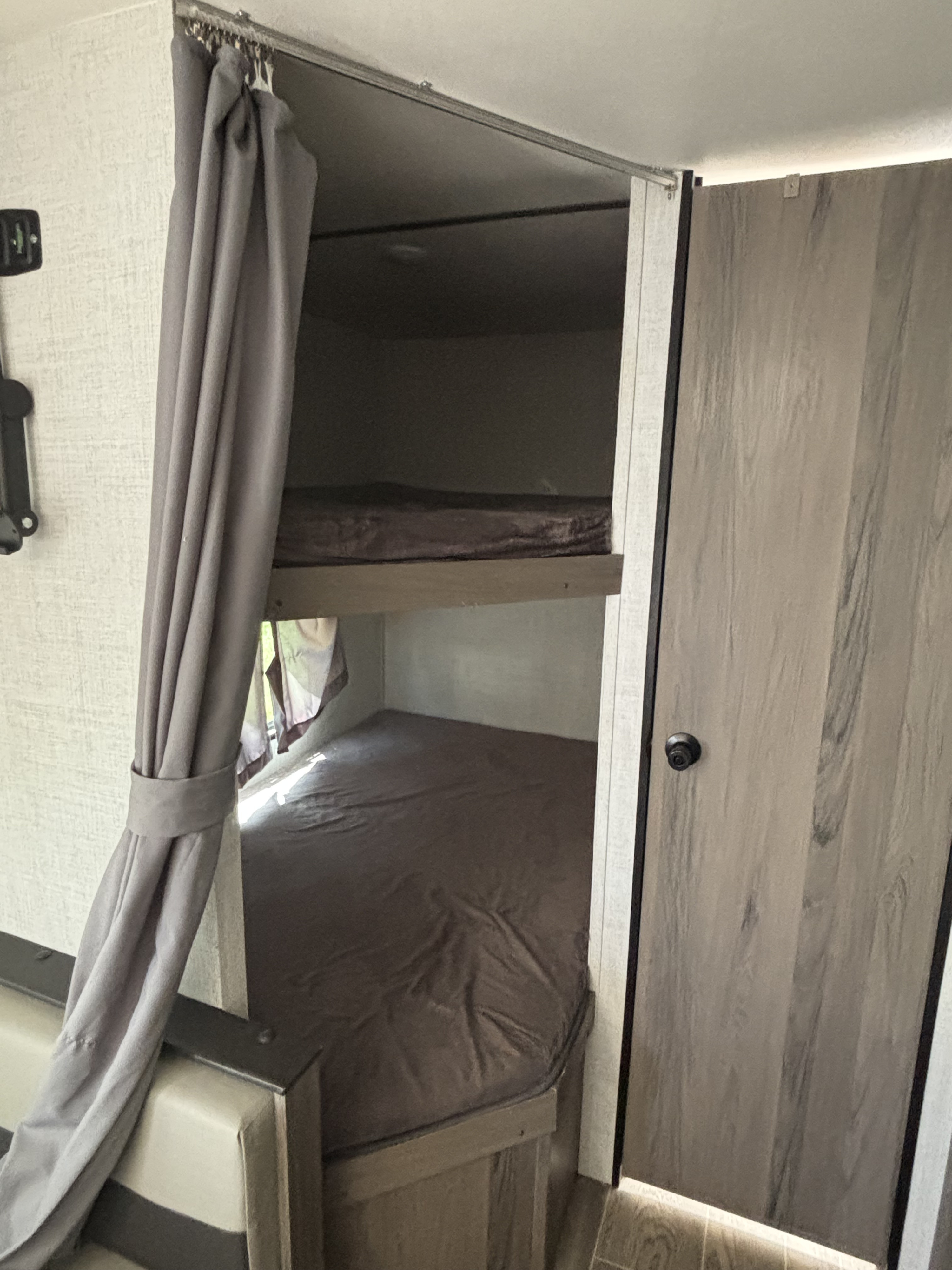 Cozy RV rental bunk beds, with dark mattresses partially visible behind a gray privacy curtain.. Gulf Stream Enlighten 2021
