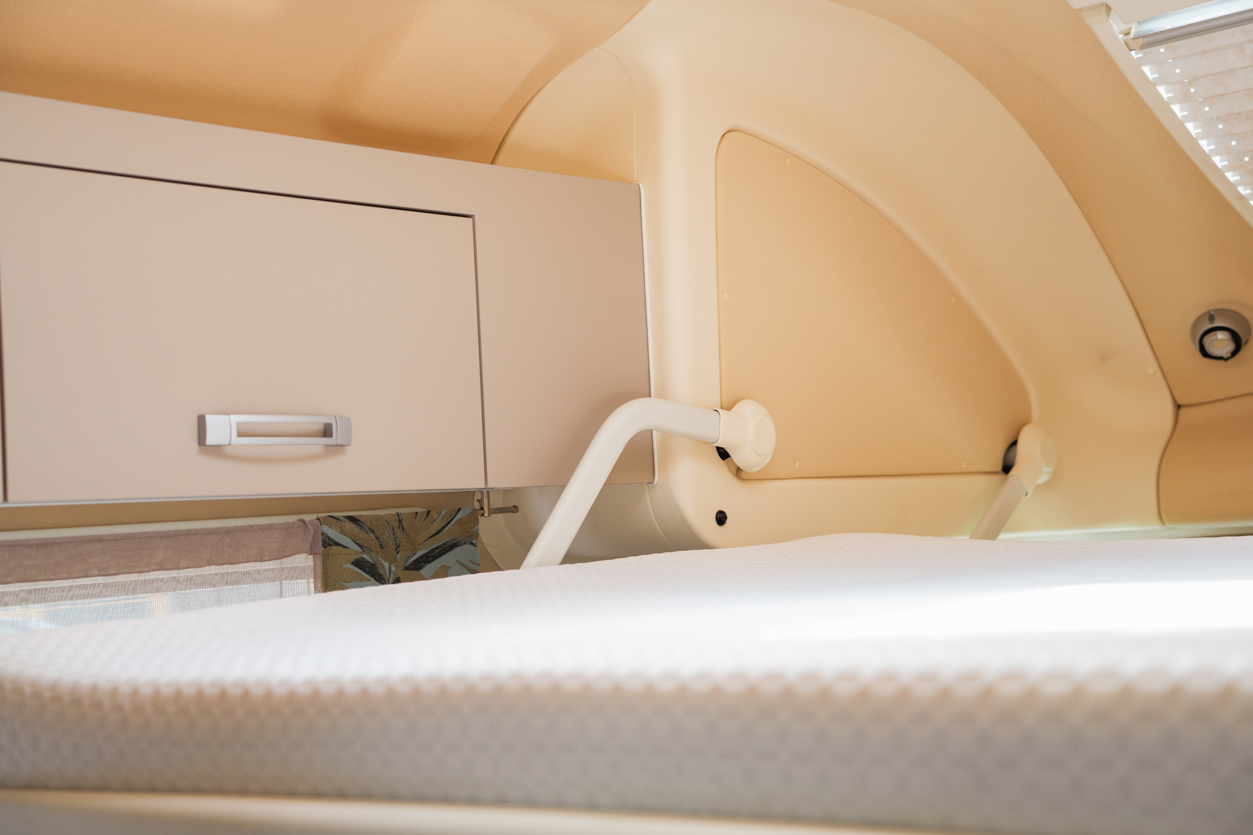 RV rental interior: Modern sleeping area with white mattress, overhead storage, and curved walls, featuring bed support arm.. WINGAMM OASI 540 2025