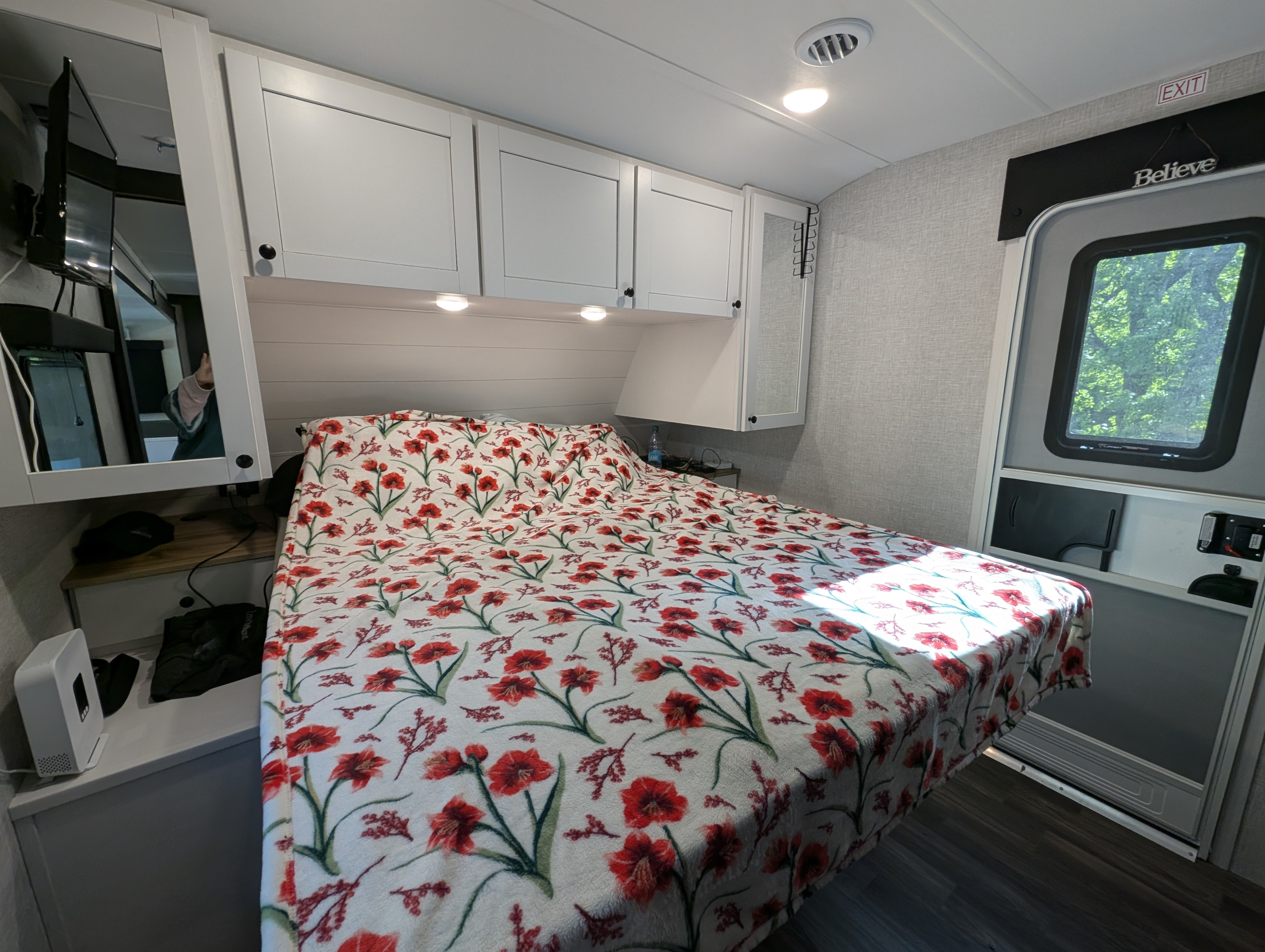 Bright RV rental bedroom features a comfy bed with a red floral blanket, white cabinets, and an exit door. Perfect for travel.. Open Range 252RB 2025