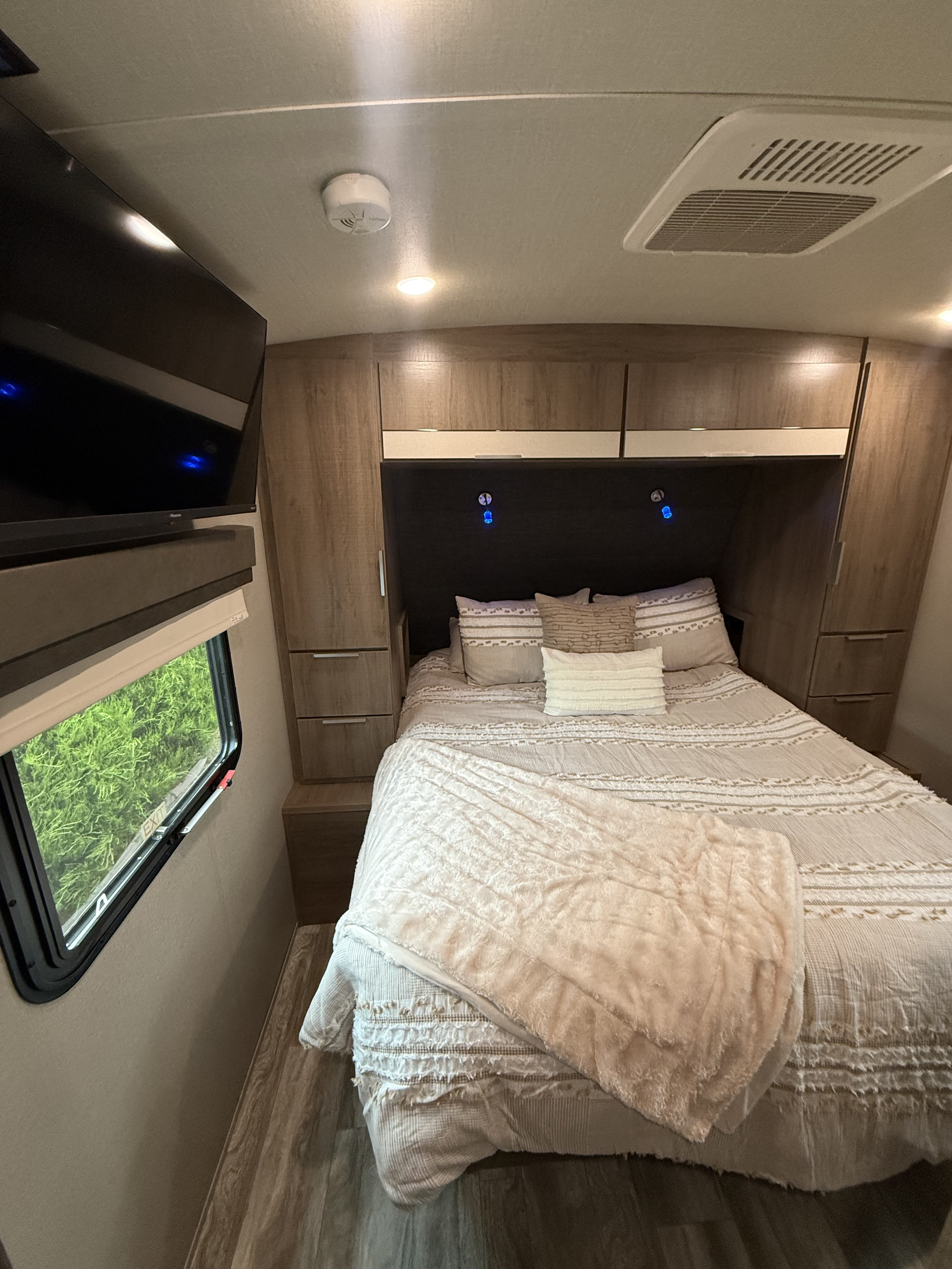 Cozy RV rental bedroom with a comfy bed, mounted TV, built-in storage, and window.. Grand Design Imagine 2021