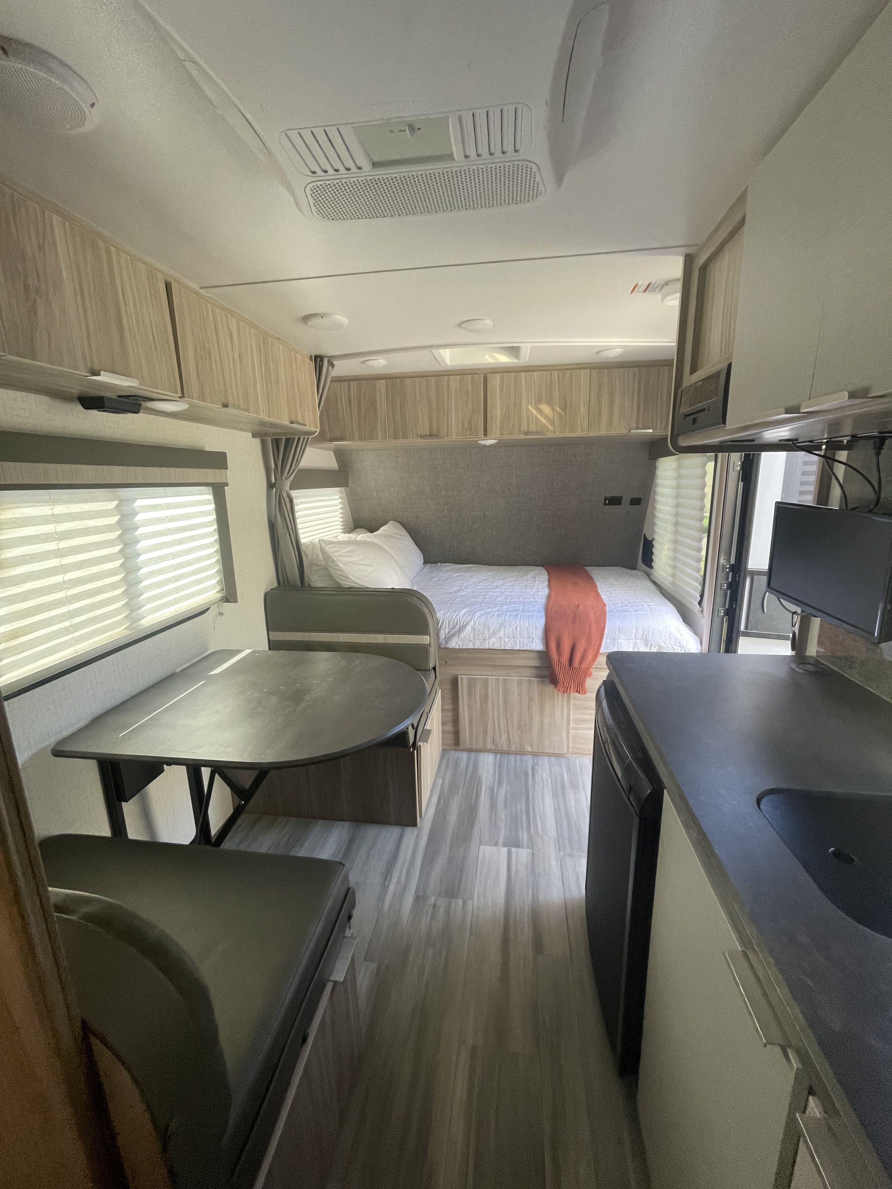 Cozy rv rental interior: features a comfortable bed, convertible dinette, and a compact kitchen area with light wood accents.. Winnebago Micro Minnie 1700BH 2021