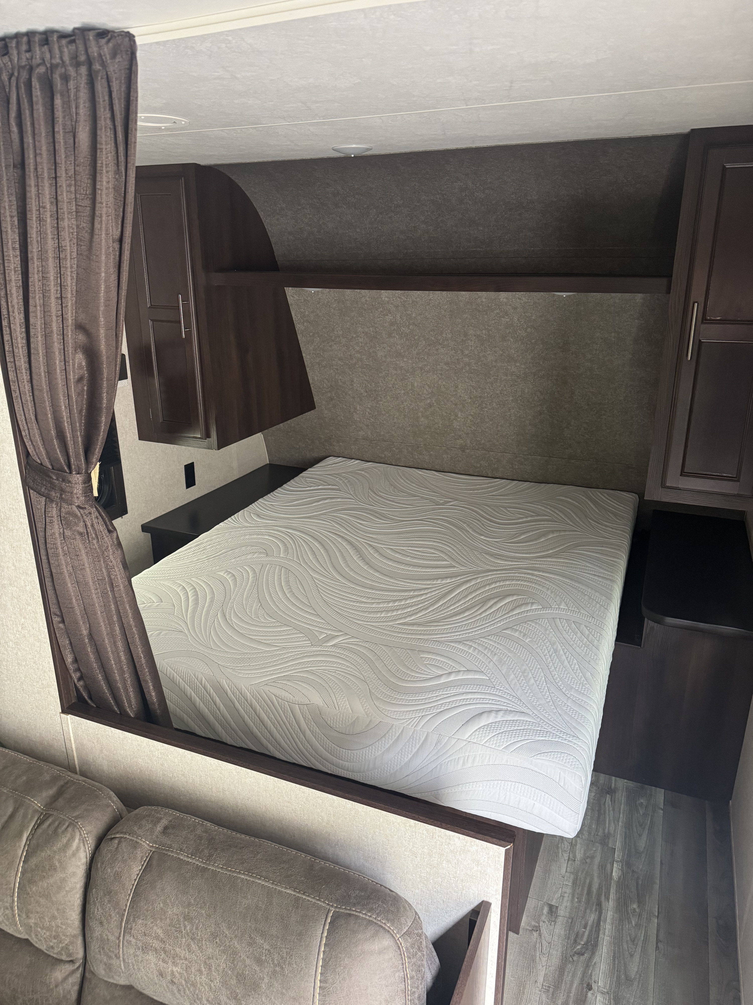 Cozy RV rental bedroom featuring a patterned mattress, dark cabinetry, and brown drapes.. Jayco Jay Flight SLX 2019