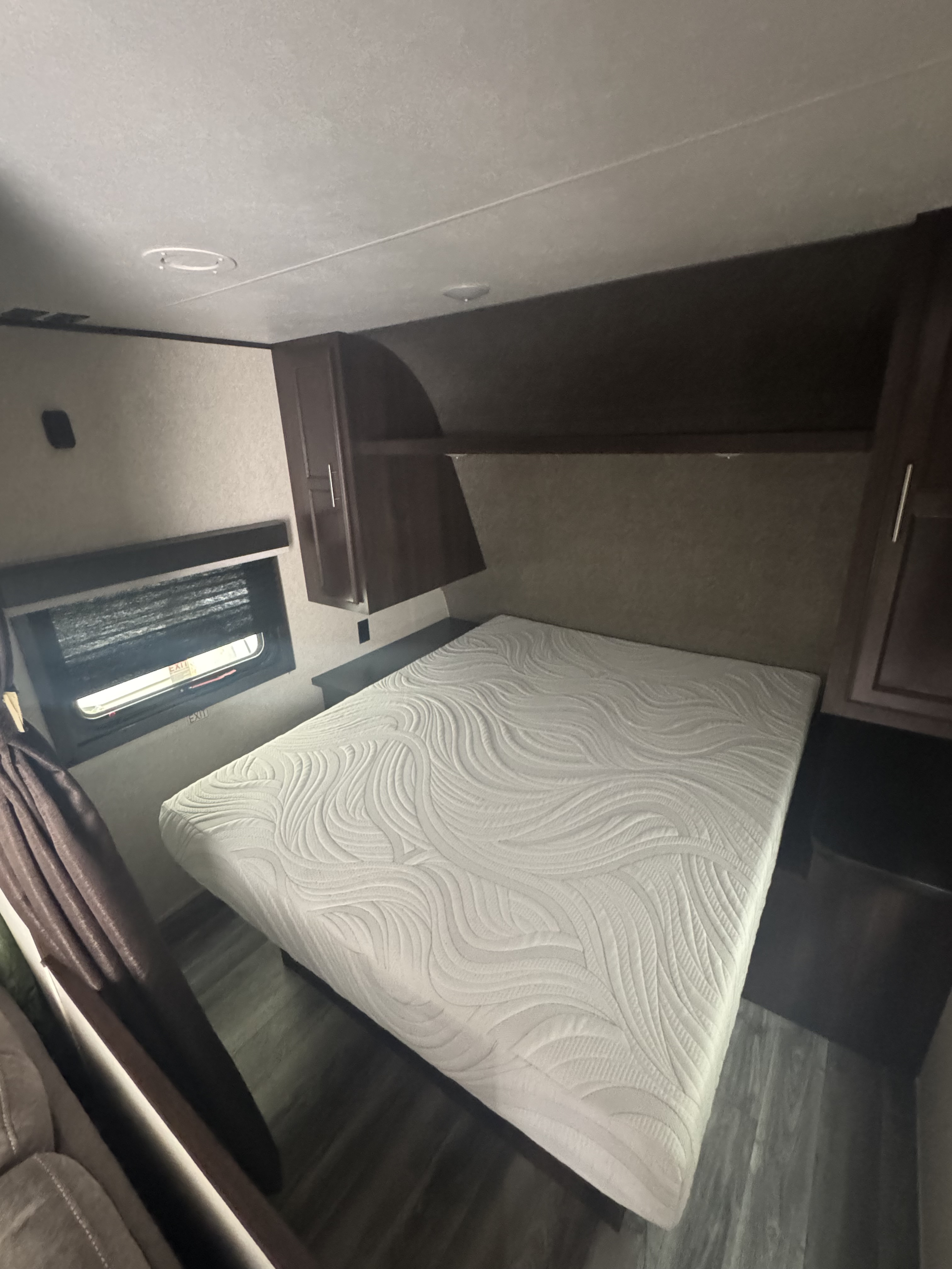 Cozy RV rental bedroom featuring a white mattress, overhead dark wood cabinets, and a window with blinds.. Jayco Jay Flight SLX 2019
