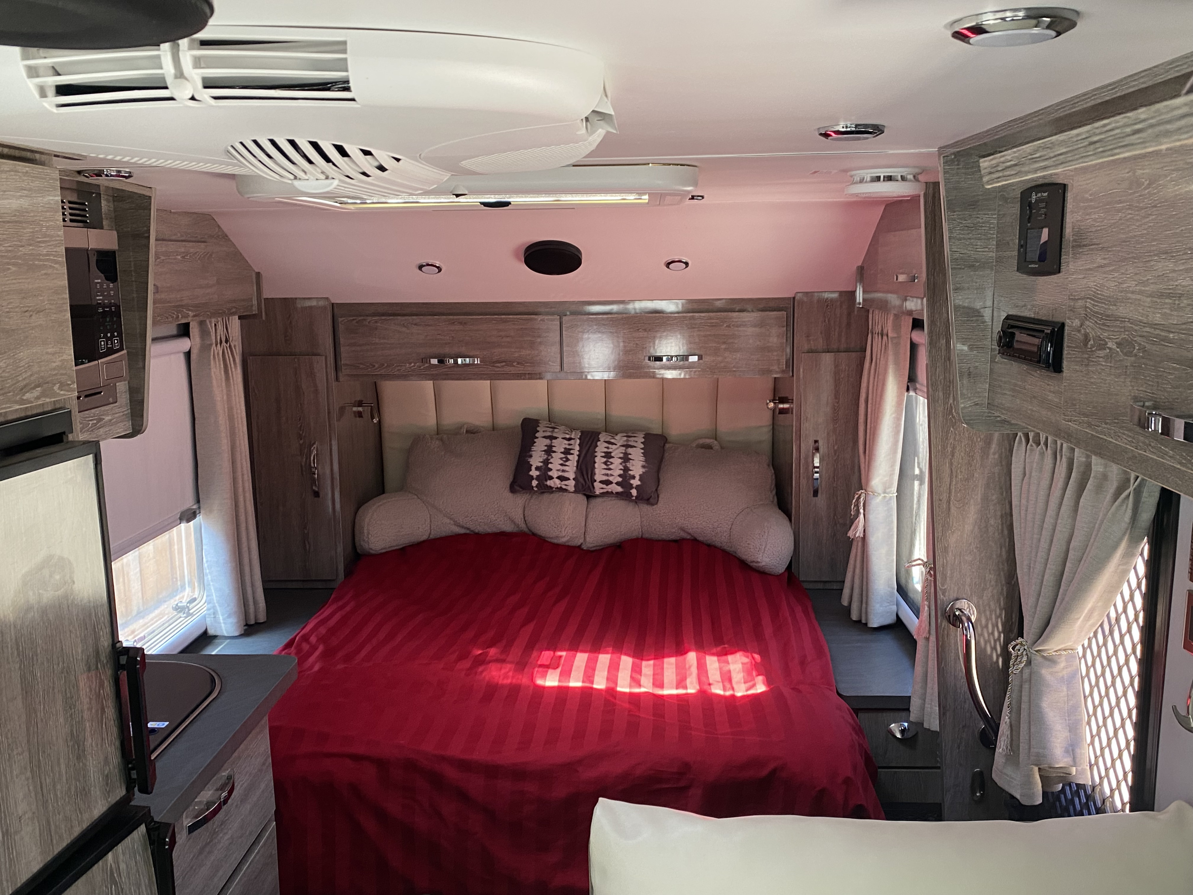 RV rental interior showcasing a comfortable bedroom with red sheets, overhead cabinets, and a compact kitchen setup.. Black Series Black Series Trailer 2021