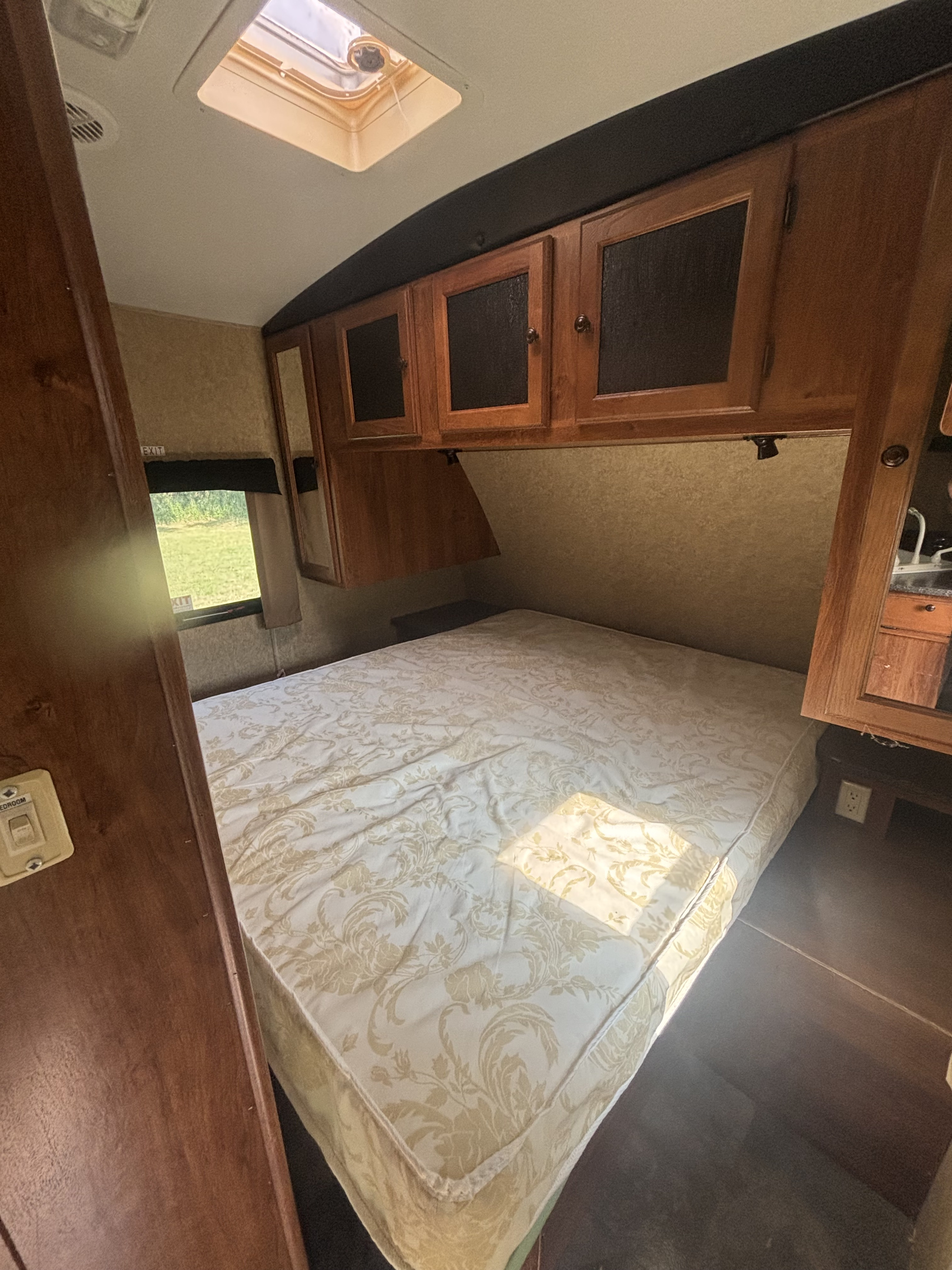 Inside an RV rental: a cozy bedroom with a patterned bed, overhead cabinets, a skylight, and a window view.. Heartland RVs Wilderness 2012