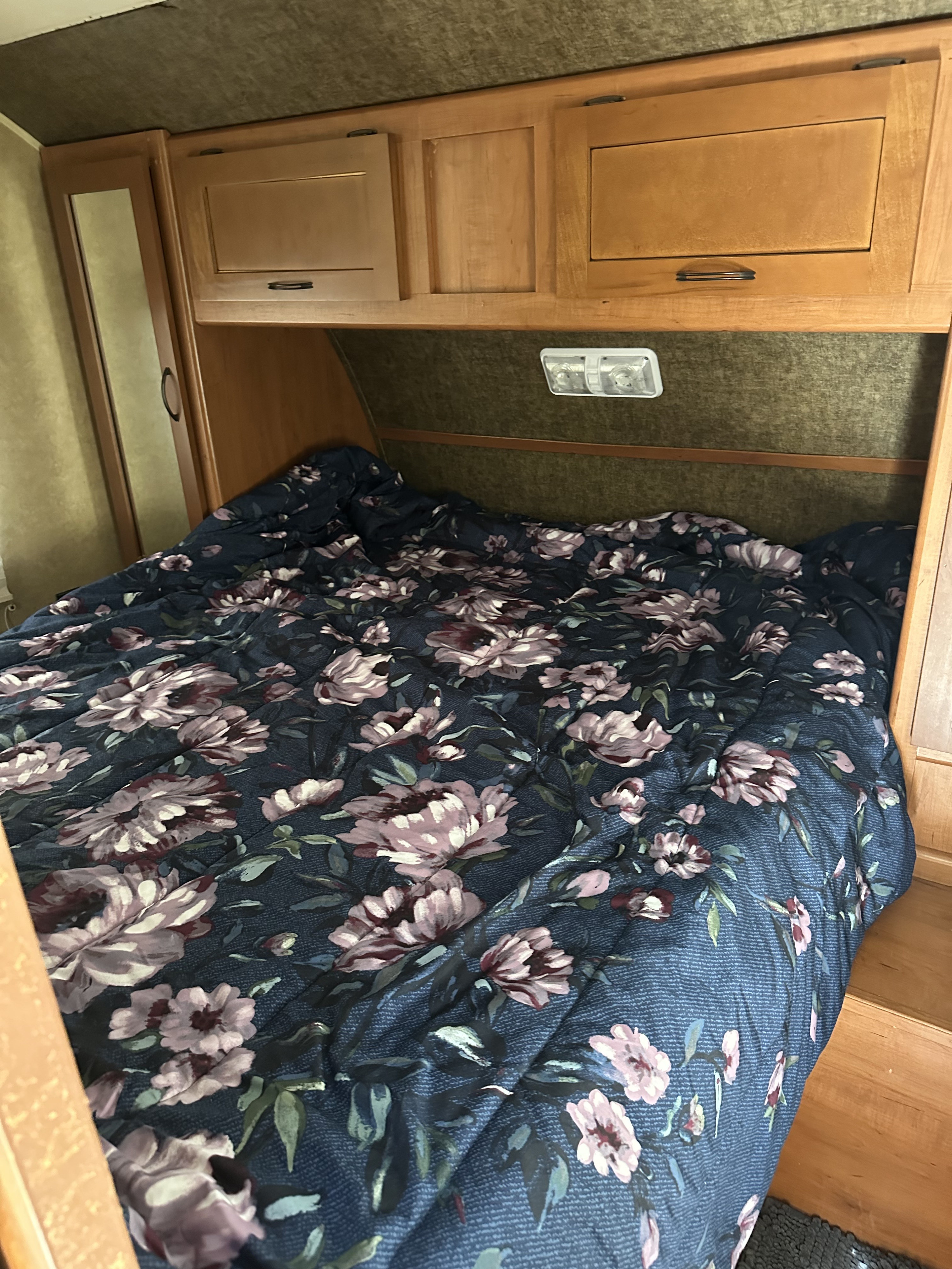 Cozy RV rental bedroom with a dark blue floral comforter and ample wooden overhead storage. Perfect for a camper's retreat.. Forest River Cherokee Grey Wolf 2015