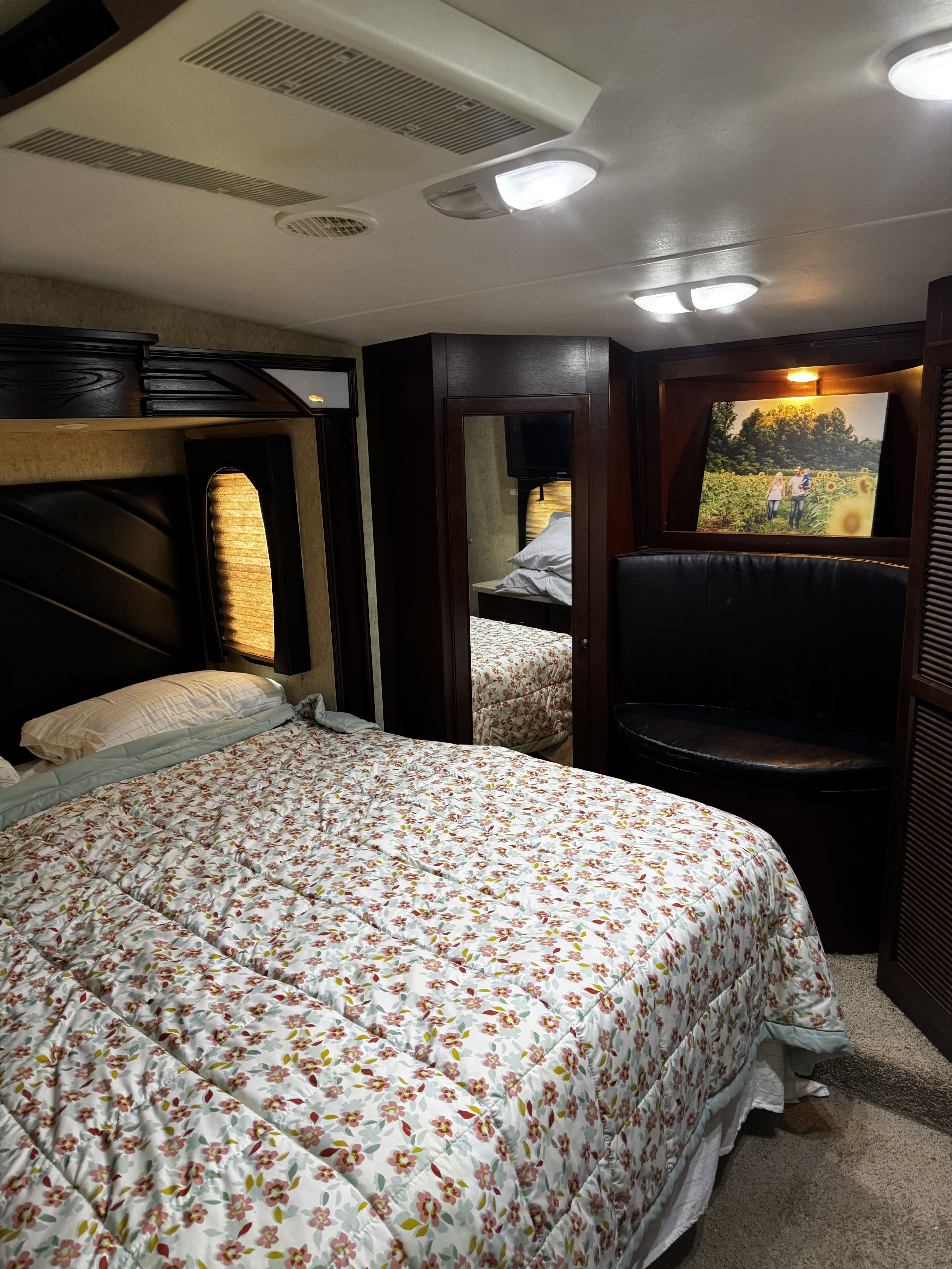 Inside an RV rental, a welcoming bedroom features a floral bedspread, dark wood furniture, and soft lighting.. Heartland Cyclone 2013