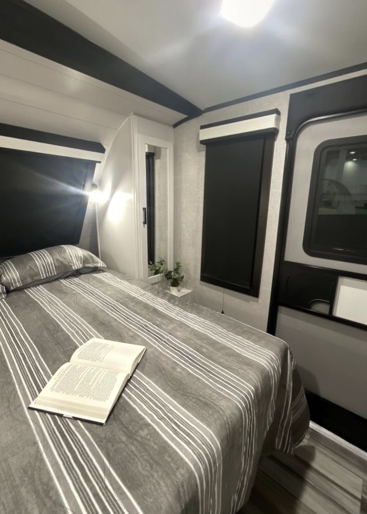 Relaxing RV rental bedroom: striped bed with a book, bright lighting, and modern, functional design.. Jayco White Hawk 2024