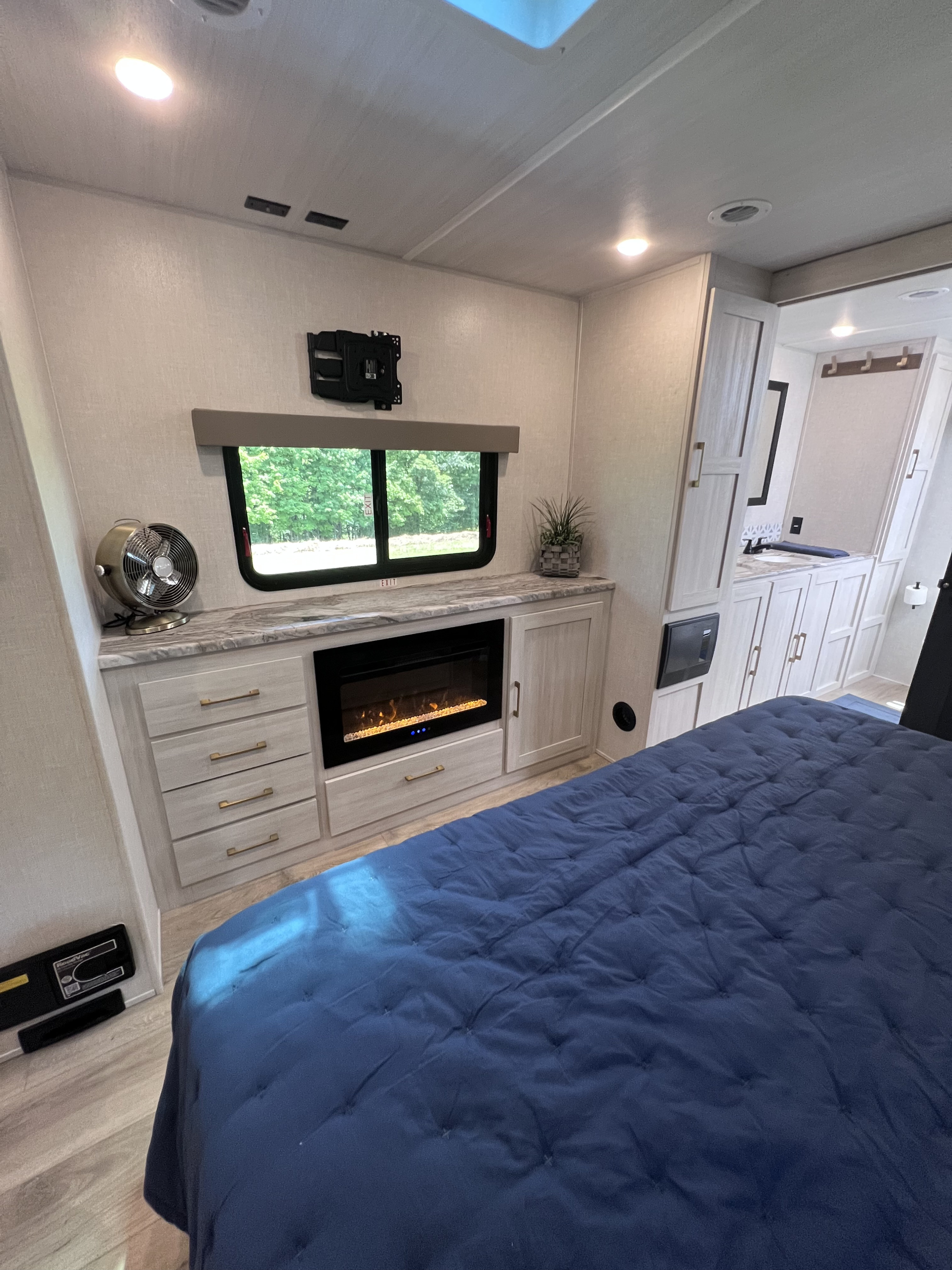 Spacious and modern RV rental bedroom featuring a blue bed, electric fireplace, and glimpse of the en-suite bathroom.. Forest River Grand Surveyor 2024