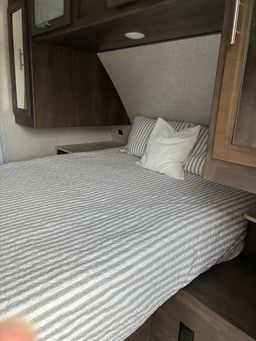 Cozy RV rental bedroom with striped bedding & white pillows. Perfect for travel & camping comfort in an RV interior.. Dutchmen Coleman Light 2021