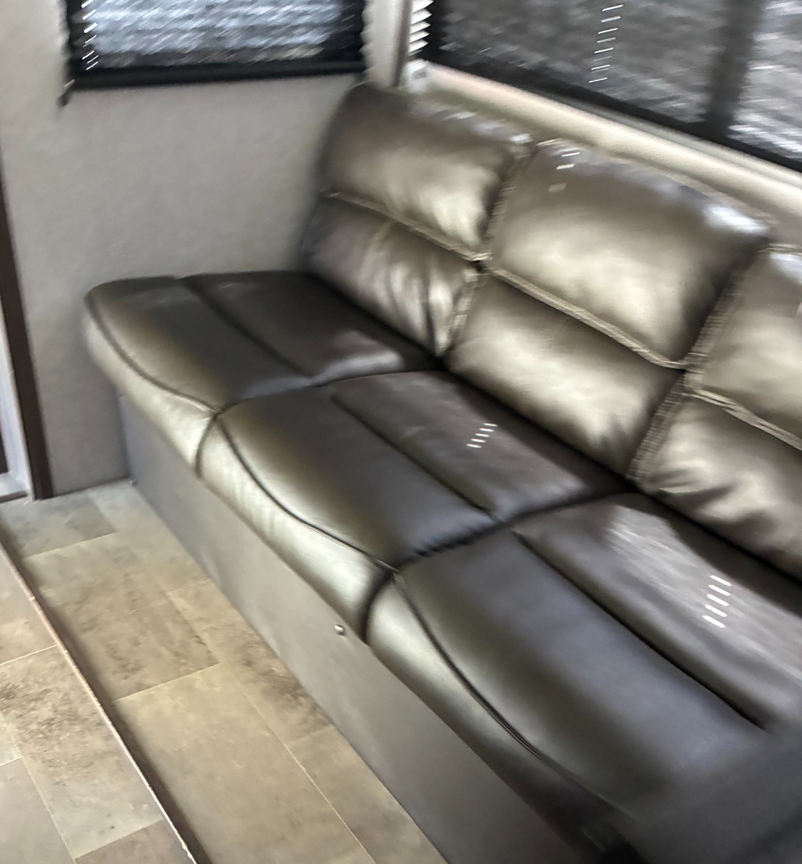 Comfortable RV rental interior featuring modern grey padded sofa, window blinds, and tile-look flooring.. Dutchmen Coleman Light 2021