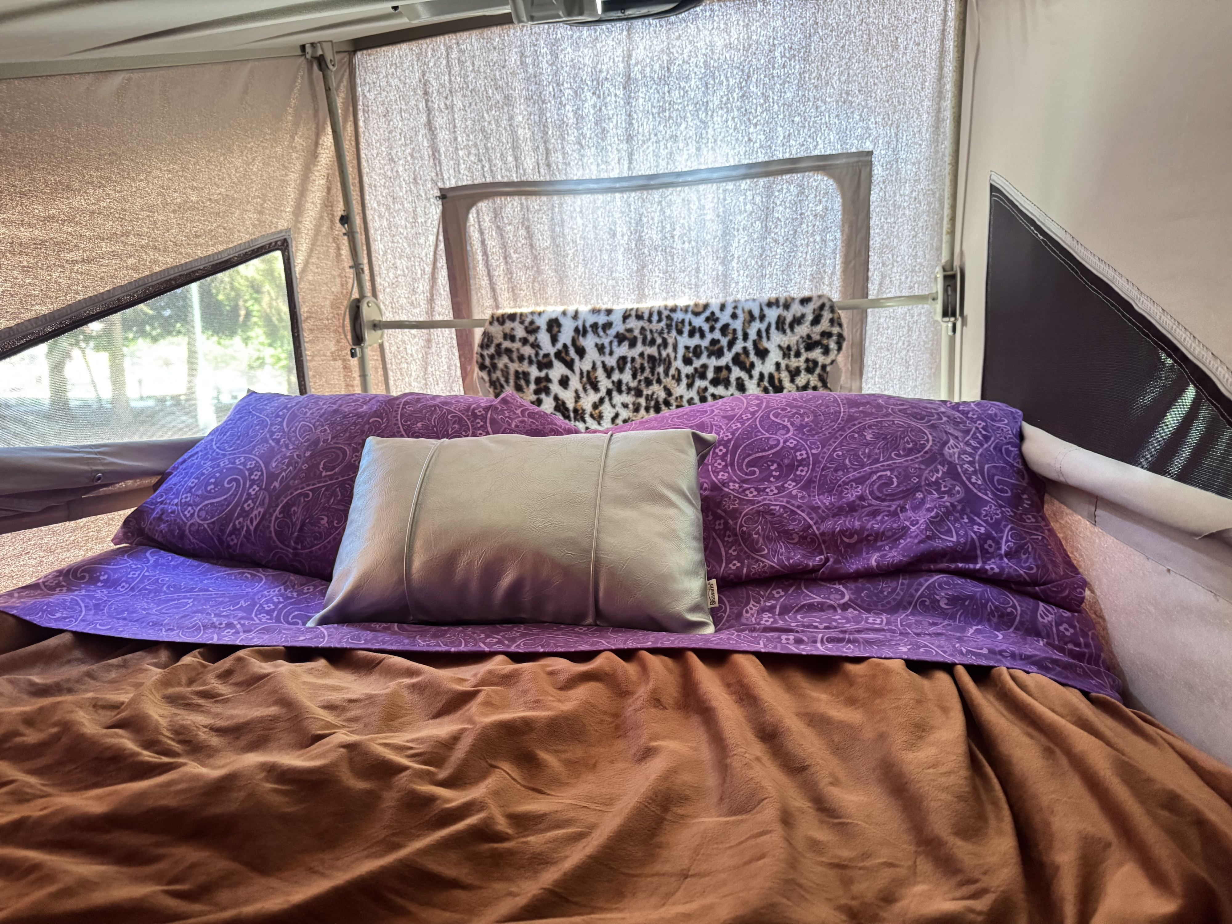 Cozy RV rental bed with purple paisley pillows, brown blanket, and leopard print throw. Enjoy nature views!. Volkswagen T3 Westfalia 1987