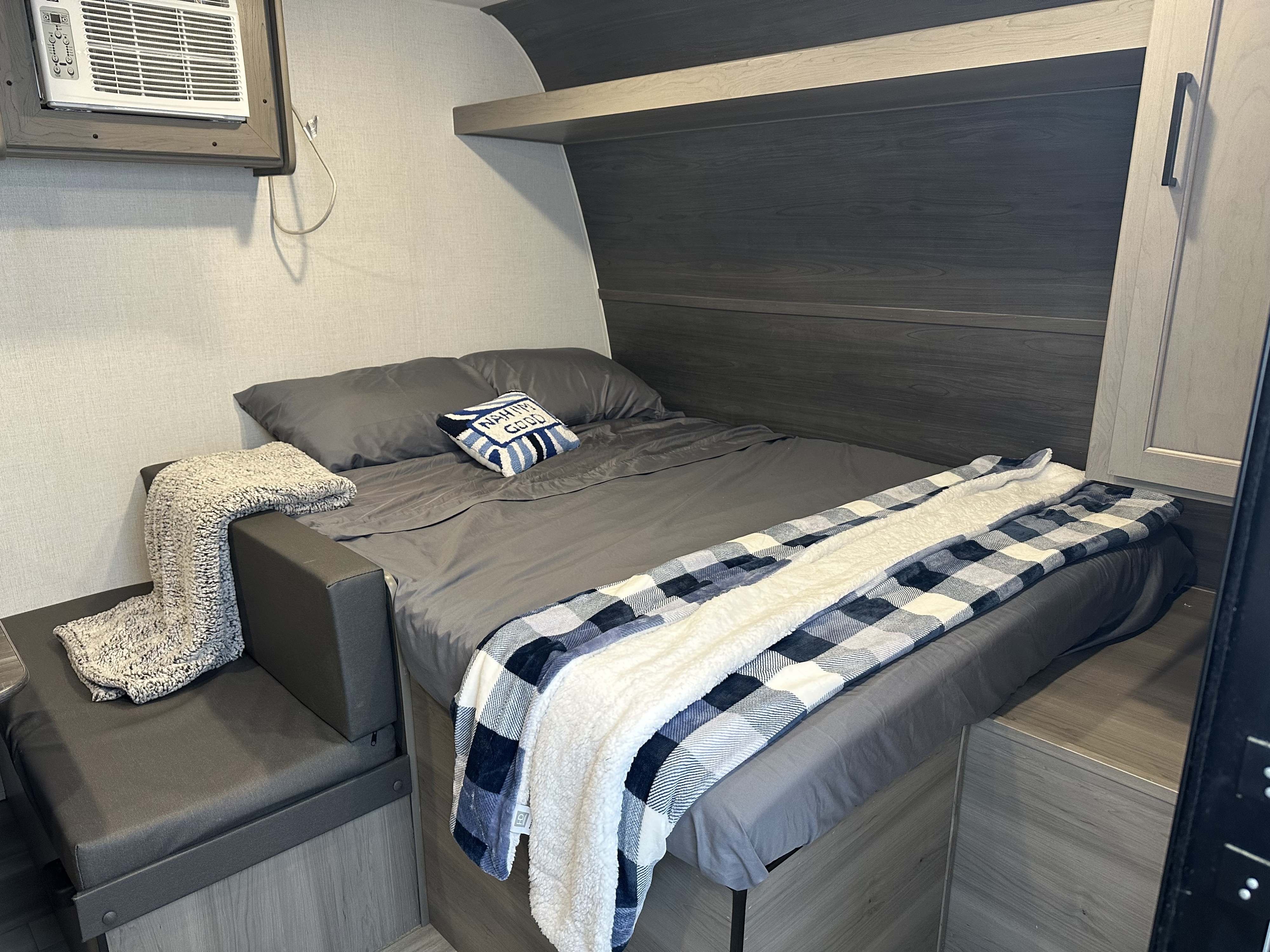 Compact and cozy RV rental bedroom featuring a comfortable bed with plaid blanket and AC unit.. Keystone RV Hideout Sport 2024