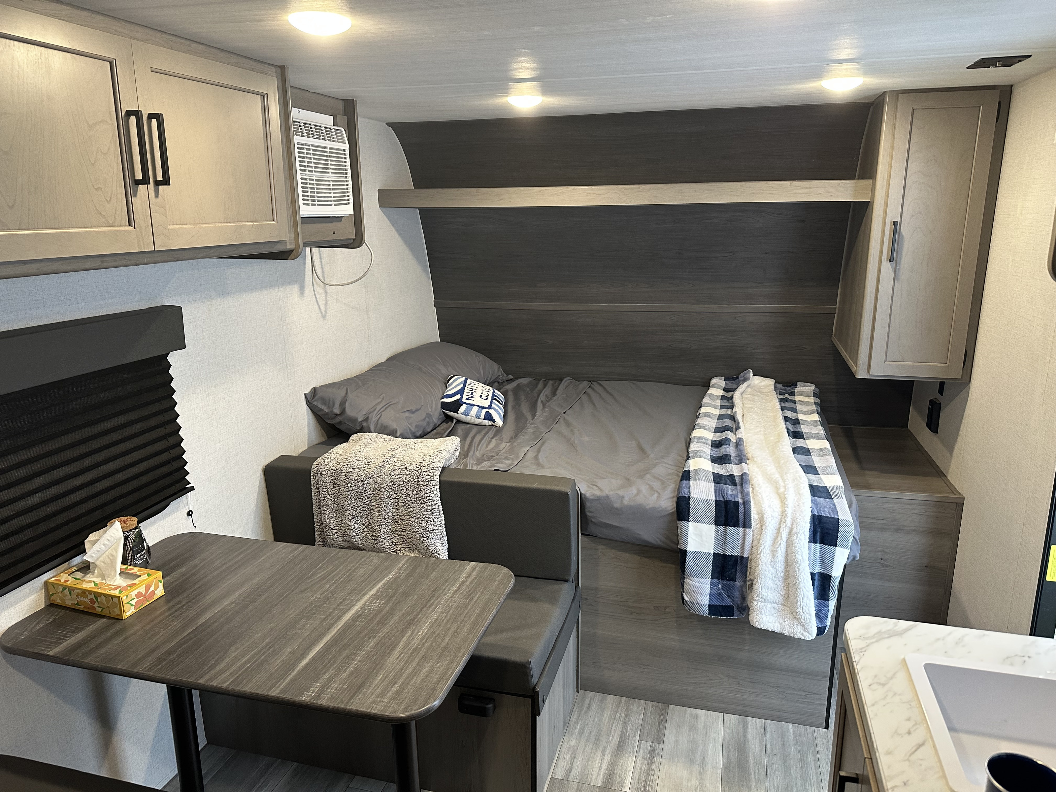 Cozy RV rental interior with a bed, dinette, overhead cabinets, AC unit, and compact sink area.. Keystone RV Hideout Sport 2024