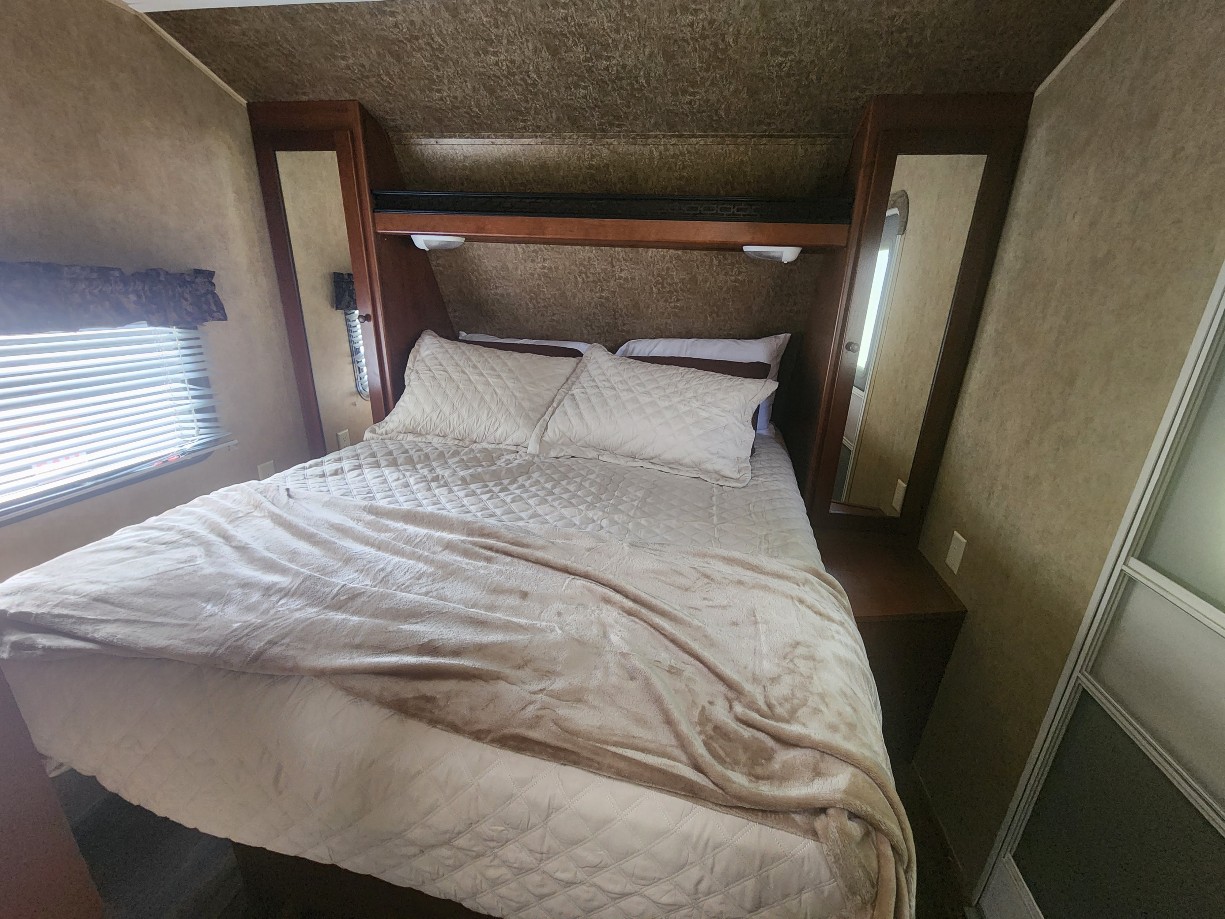 Cozy RV rental bedroom featuring a quilted bed, built-in storage, and window blinds.. Aspen Trail Aspen Trail Trailer 2013