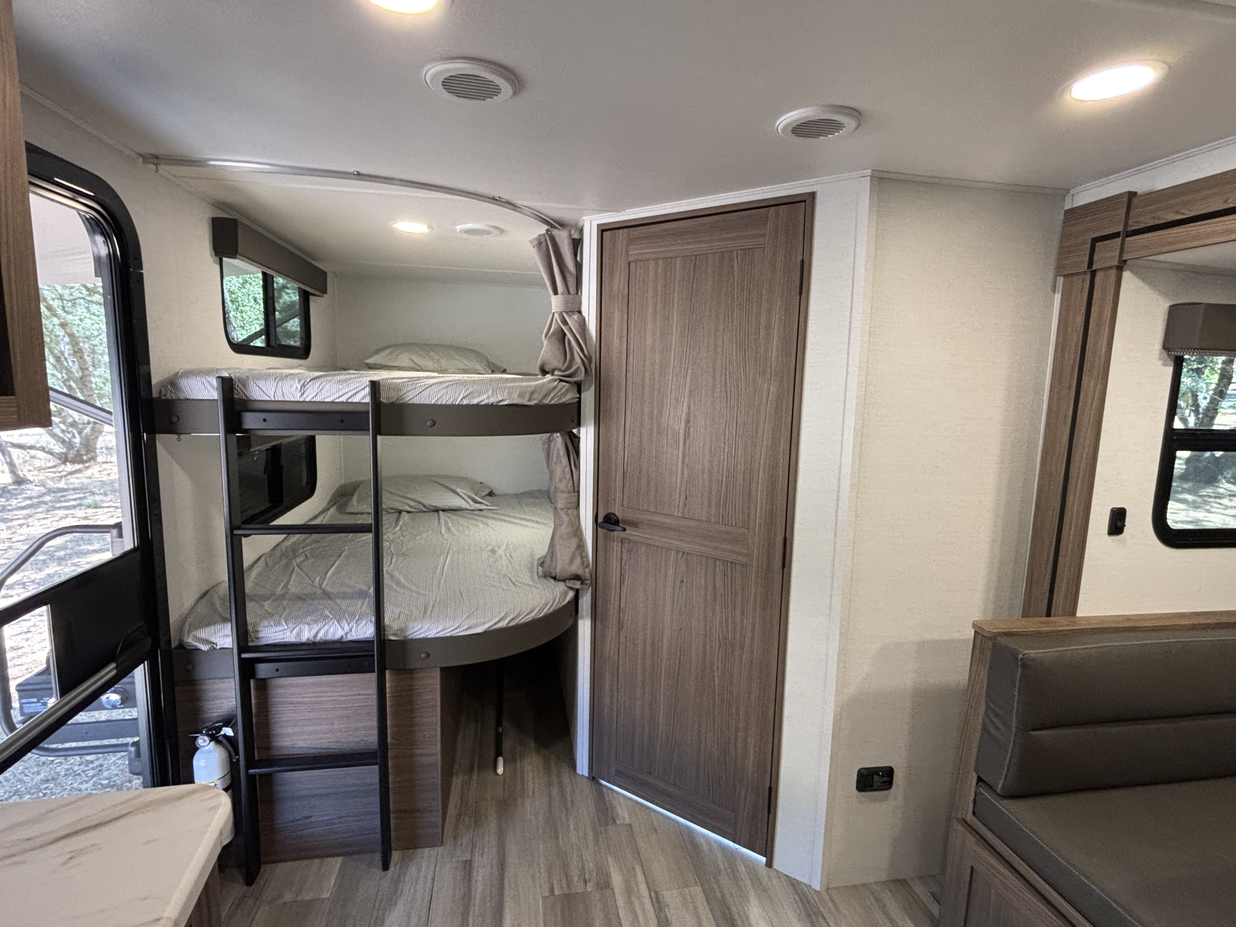 RV rental interior: bunk beds with ladder, door, and padded seating. Brightly lit with wood-look flooring.. Alliance Delta BH241 2025