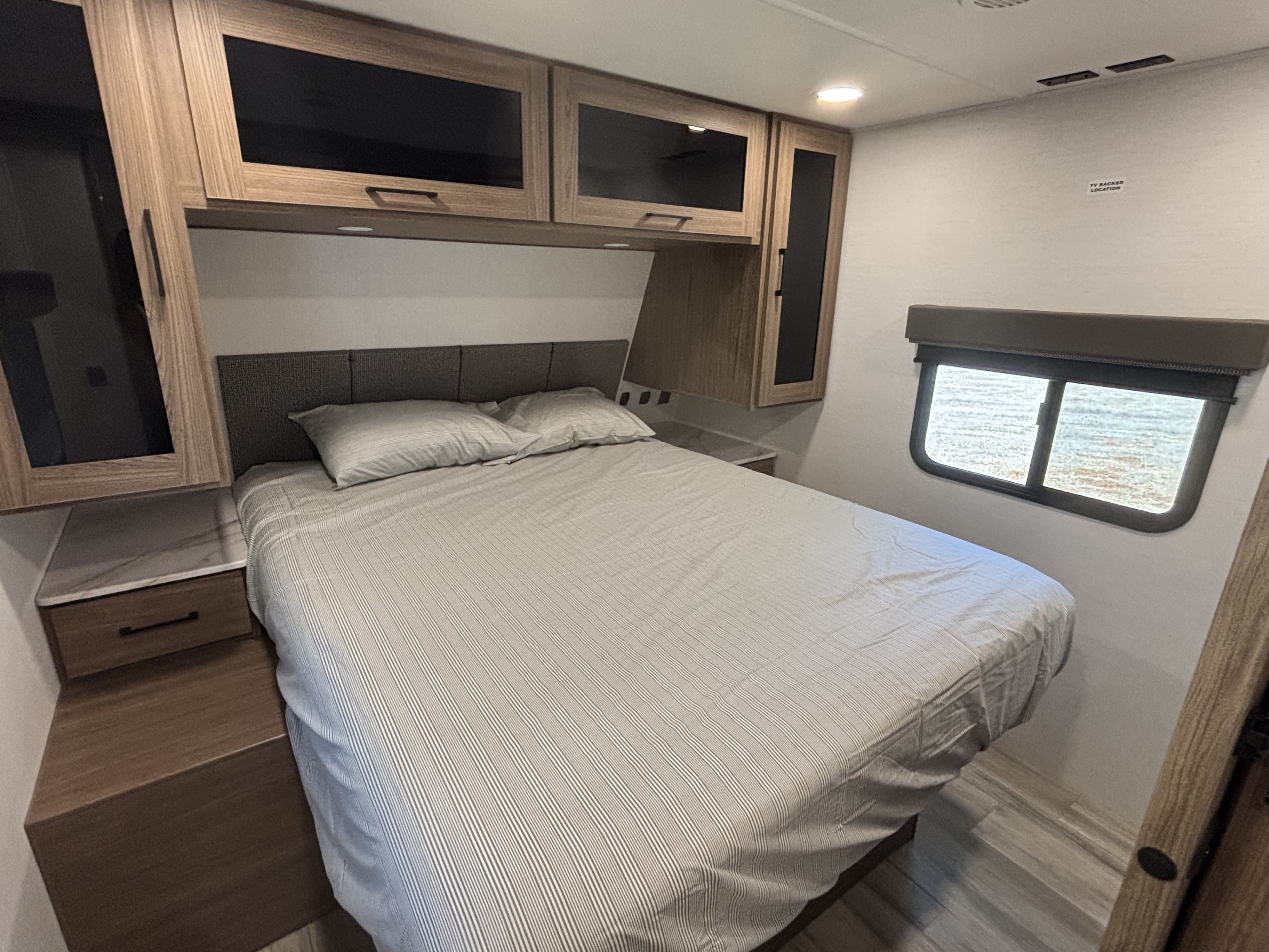 This inviting RV rental bedroom offers a cozy bed with striped sheets, convenient built-in nightstands, and ample overhead storage.. Alliance Delta BH241 2025