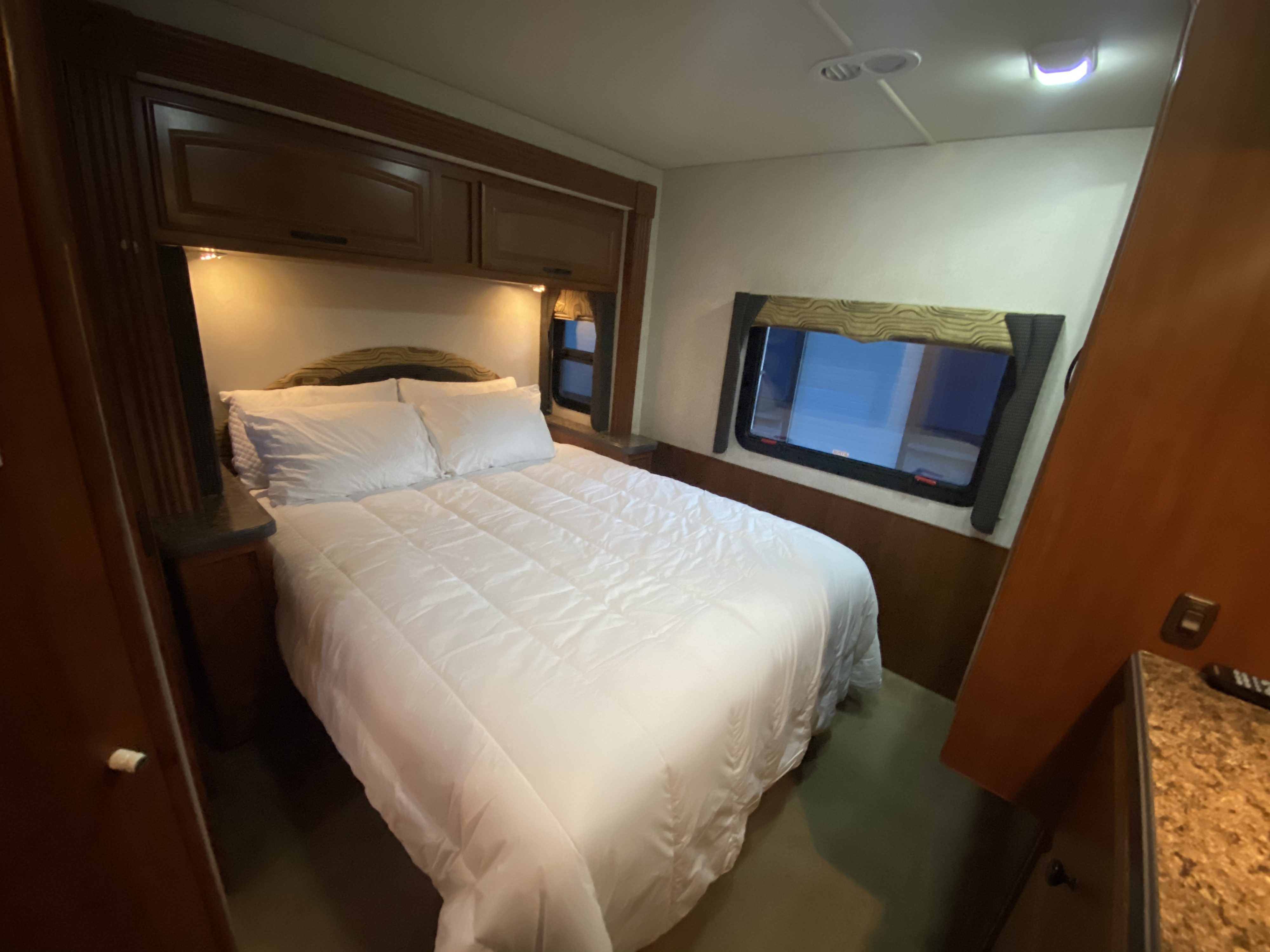 RV rental bedroom: Clean, bright space with white bedding, wooden overhead cabinets, and large windows.. Jamboree Jamboree Motorhome 2010