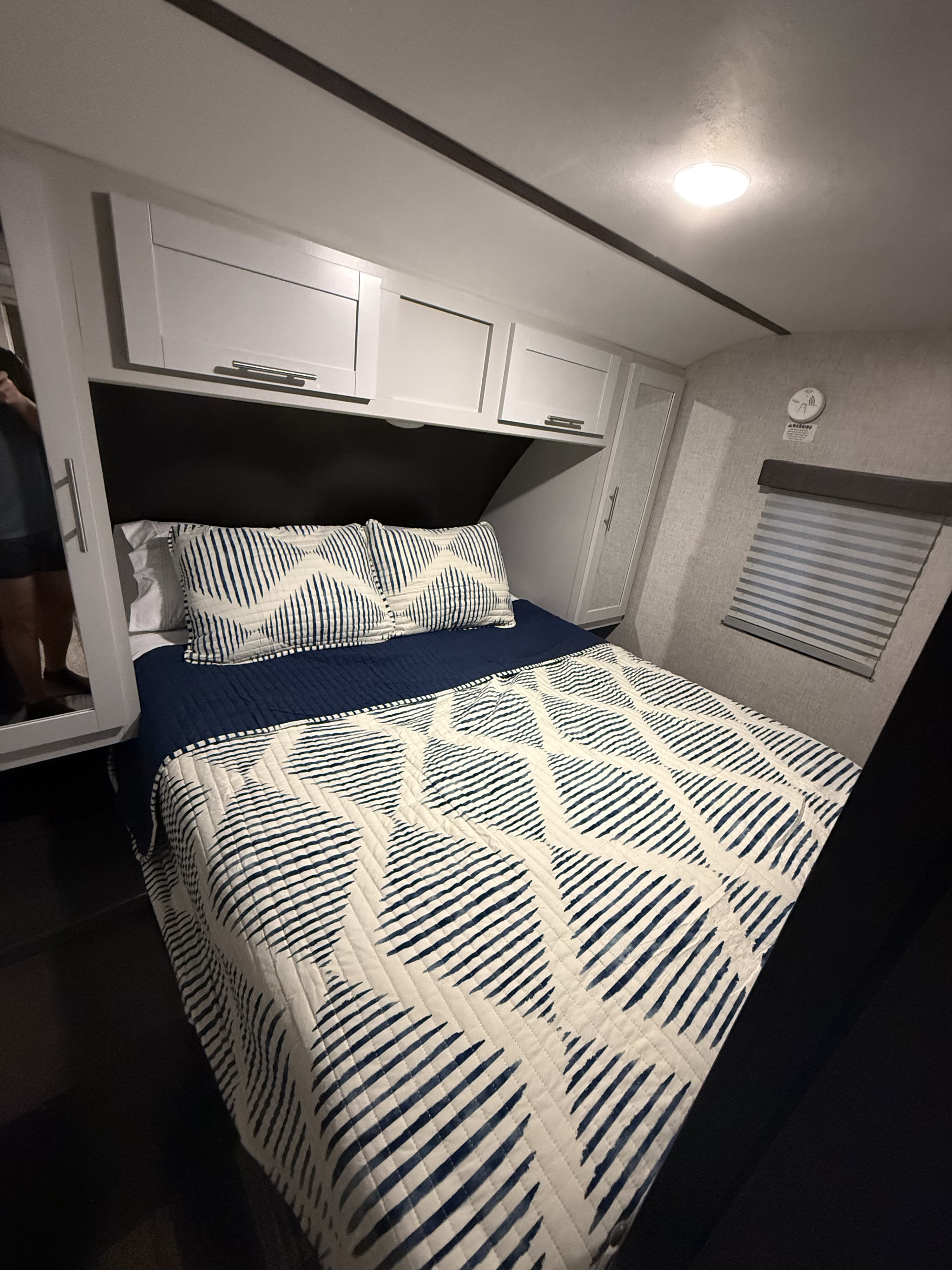 RV rental bedroom featuring a comfy bed with modern blue/white bedding, white cabinets, and a window blind.. Keystone RV Bullet Ultra Lite 2020