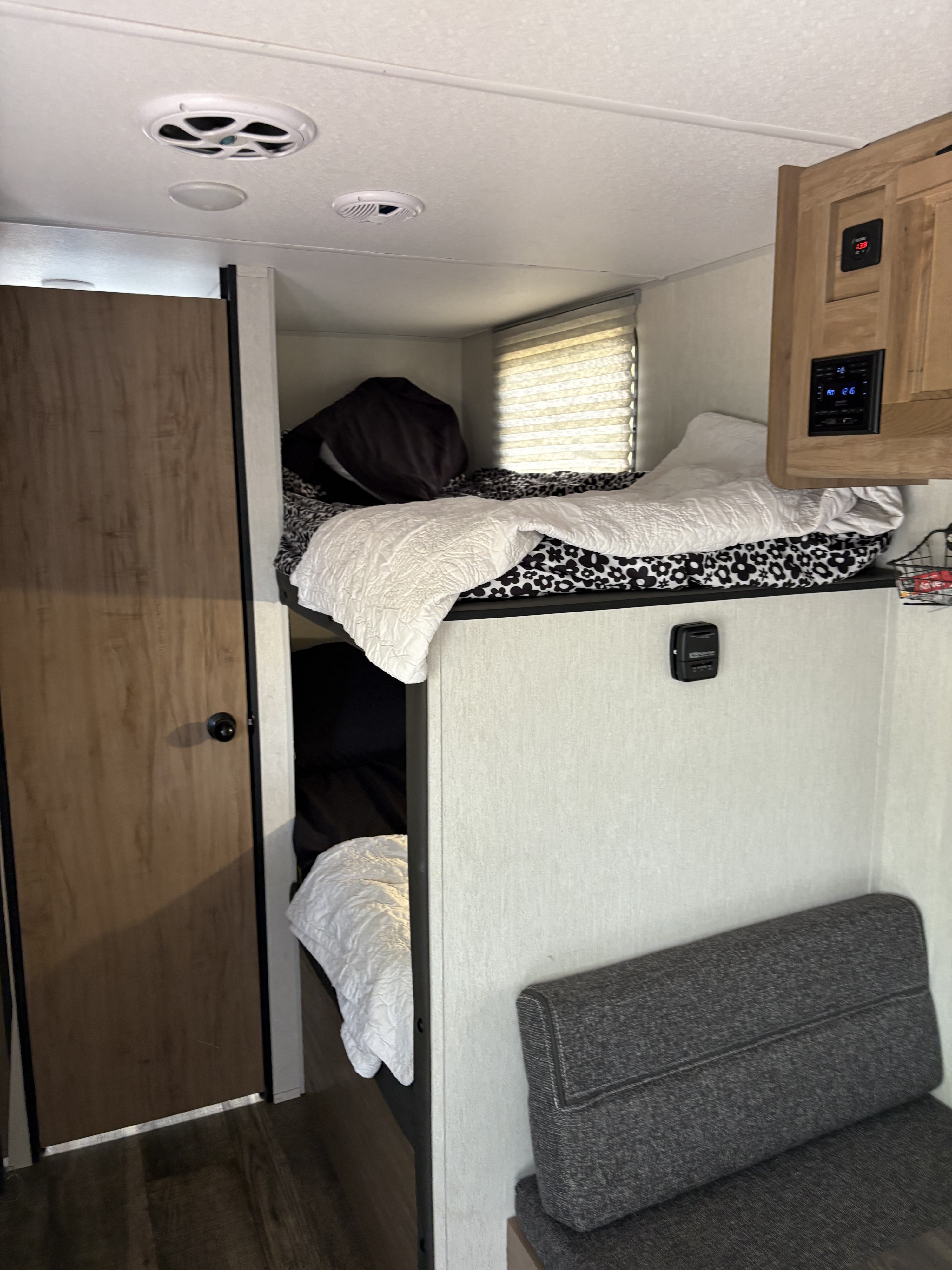 Cozy RV rental interior with stacked bunk beds, a nearby wooden door, and a small seating area.. Forest River Cherokee Wolf Pup 2024