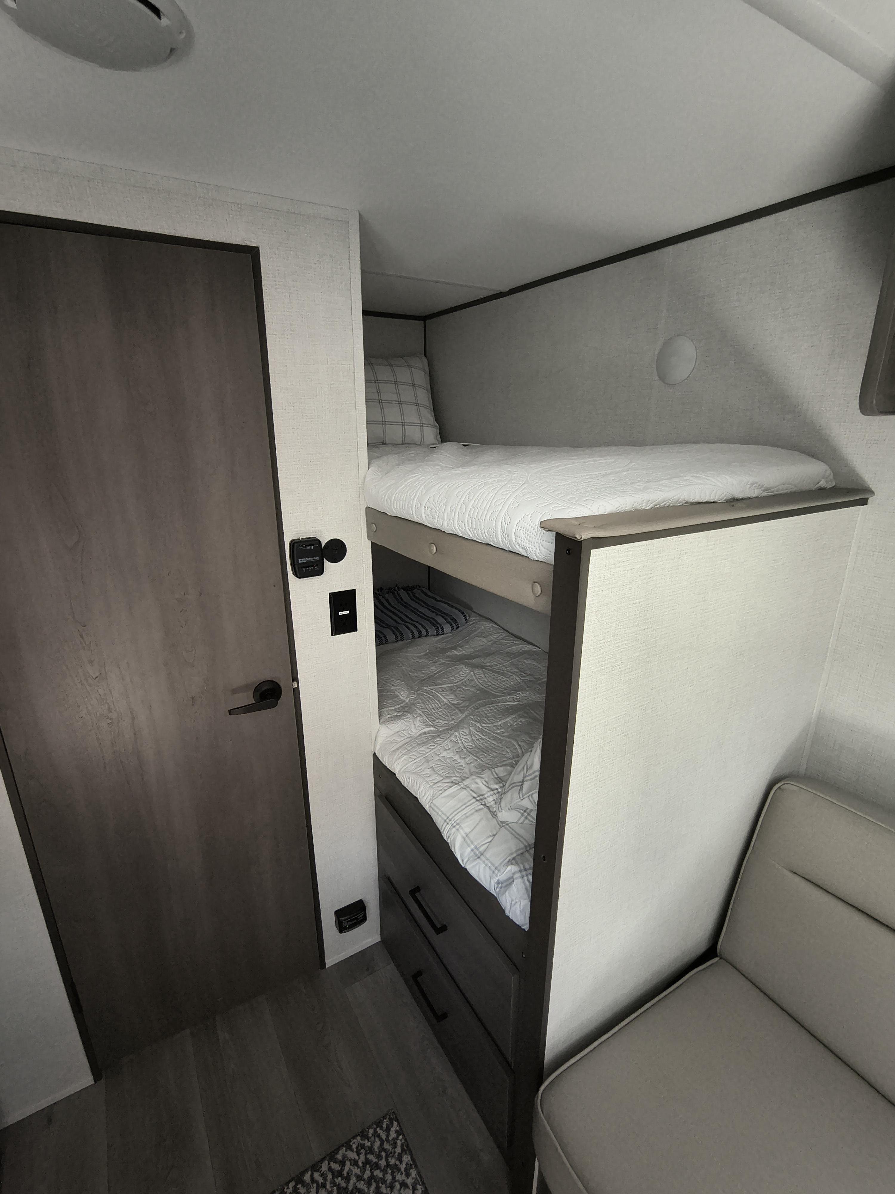 RV rental interior: light-colored bunk beds, dark wood door, and seating in a compact camper space.. Grand Design Transcend One 151BH 2026