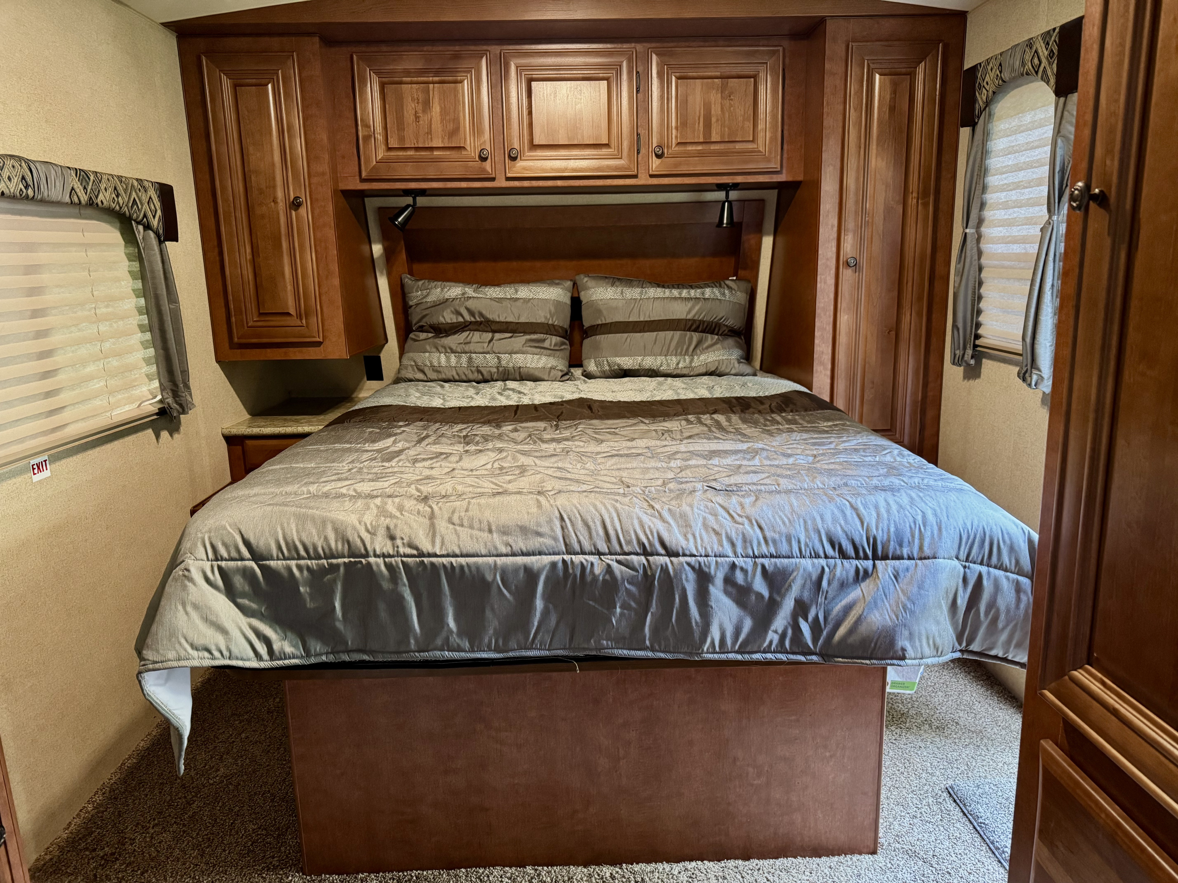 Cozy RV rental bedroom features a comfortable bed, abundant wooden storage, and windows for natural light.. Arctic Fox Classic 2017