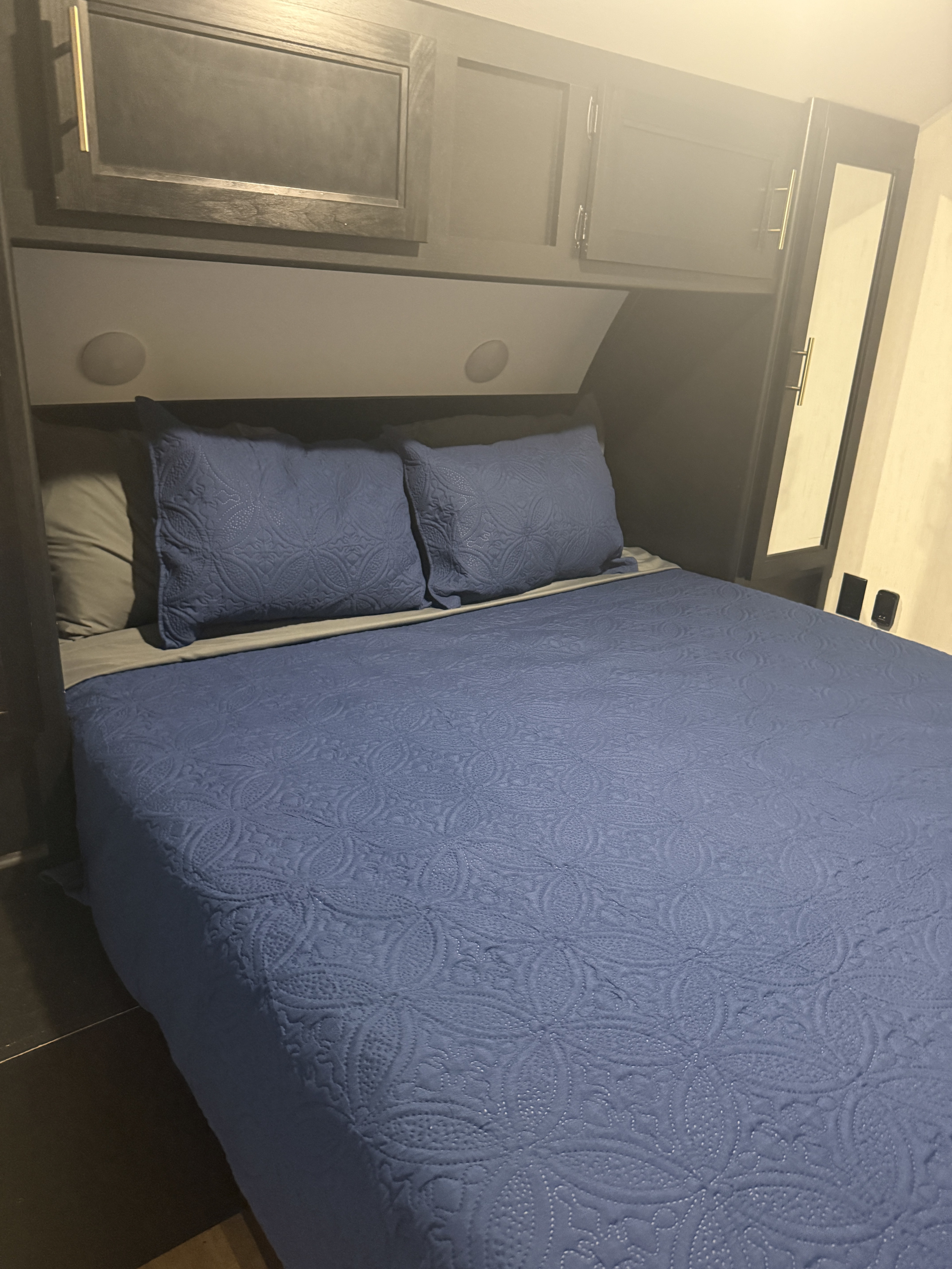 Cozy RV rental bedroom with a comfy bed, blue quilted comforter, overhead storage cabinets, and a mirrored closet.. Forest River Cherokee Grey Wolf 2022