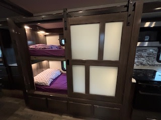 Cozy RV rental bunk beds and a frosted sliding privacy door, ideal for family travel accommodation.. Holiday Rambler Admiral 2022