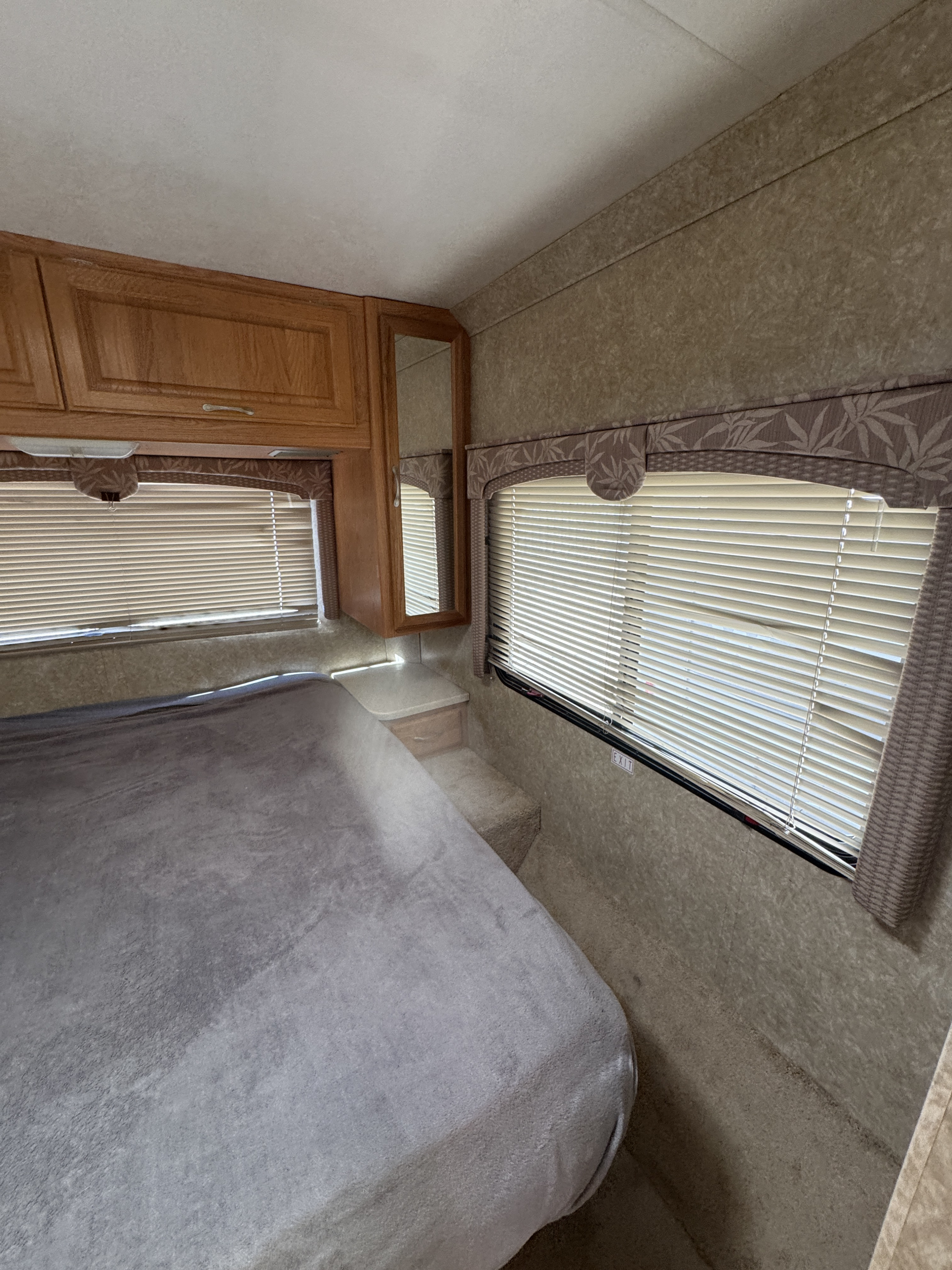 RV rental bedroom with a bed, wood cabinets, and windows with blinds. Textured walls and ceiling.. Dutchmen Express 2005
