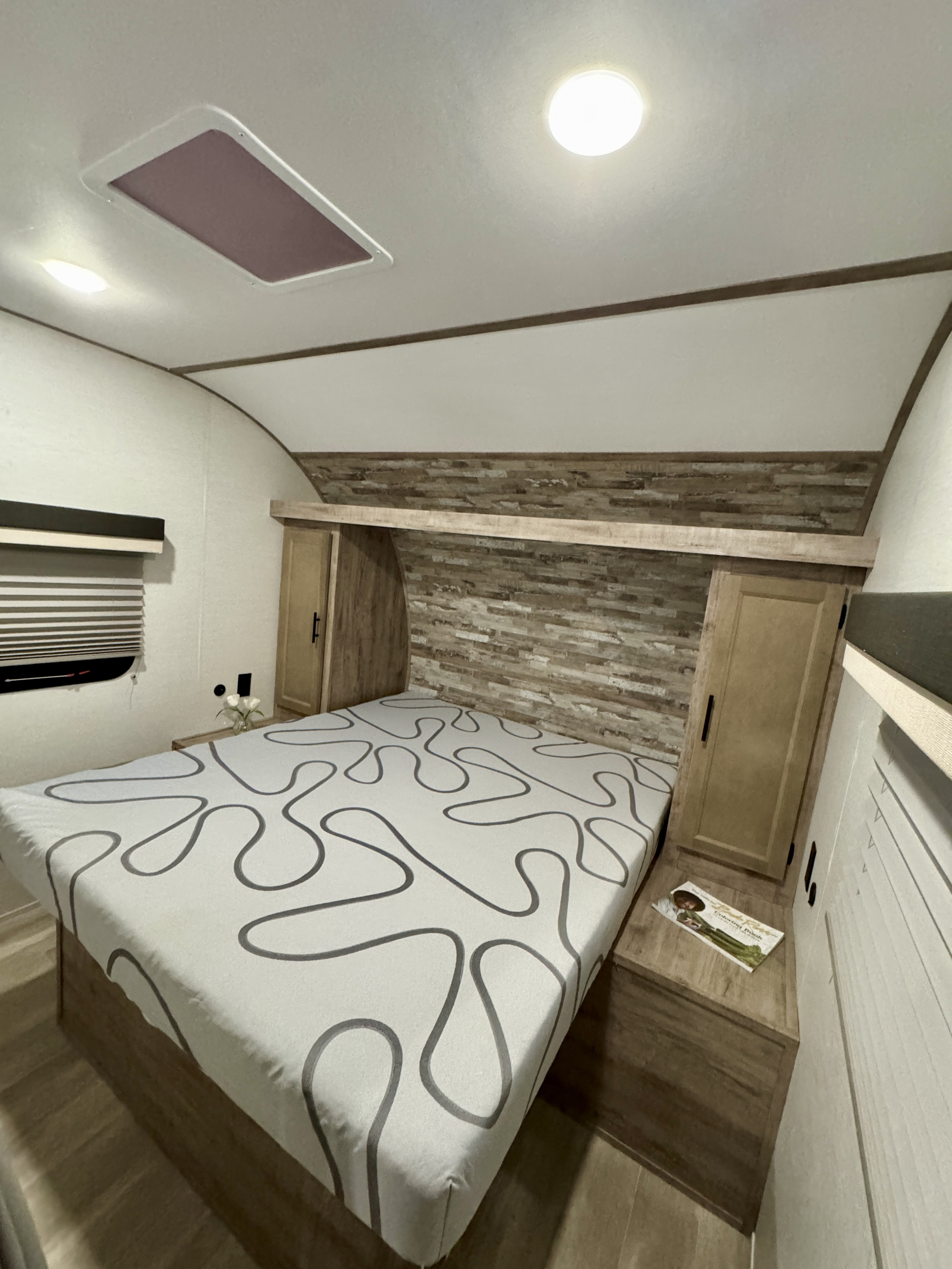 Cozy RV rental bedroom featuring a patterned bed, wood paneling, and skylight, perfect for your next adventure.. Gulf Stream Ameri-lite 2025