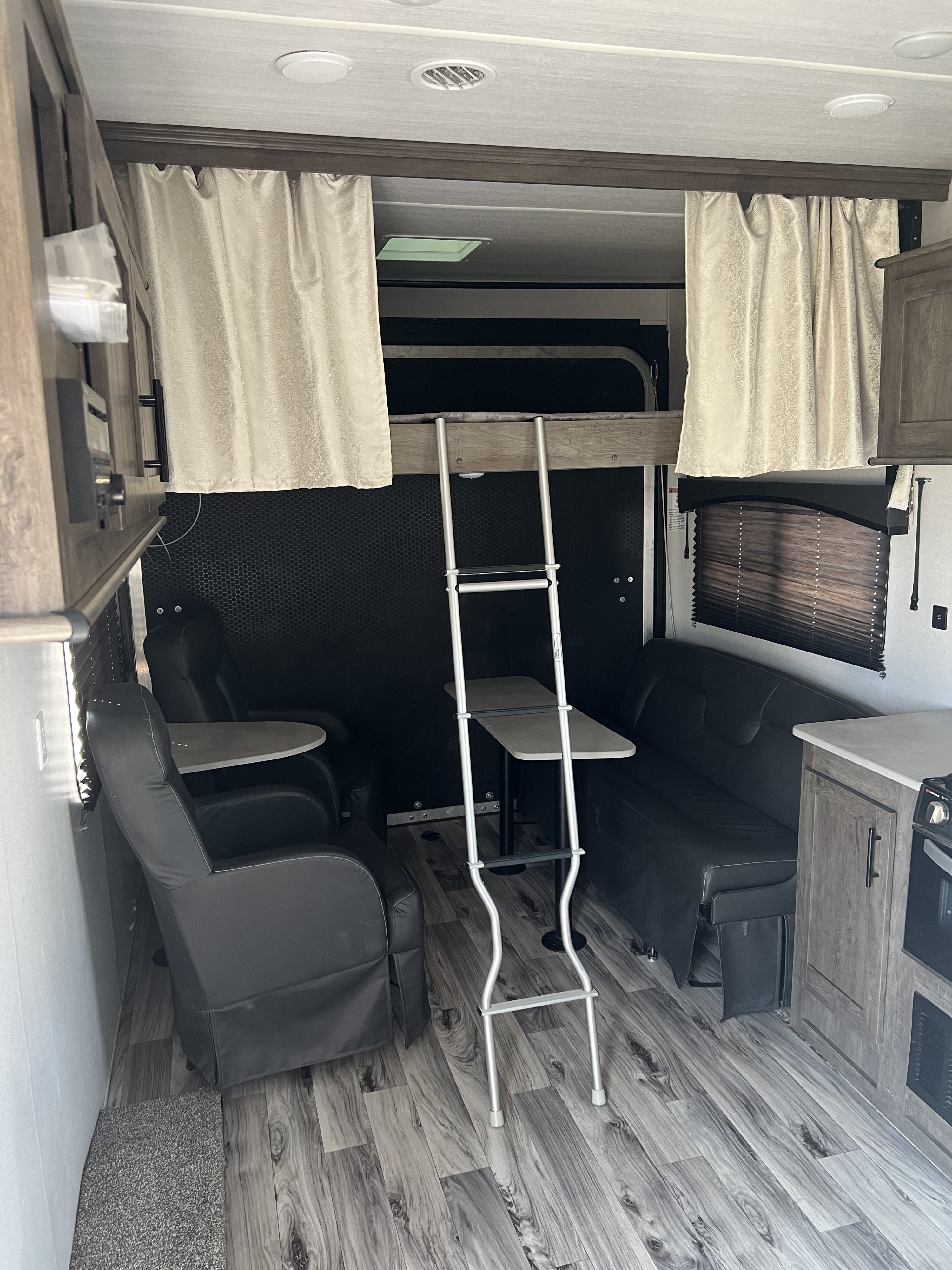 Inside an RV rental, featuring a bunk bed with ladder, two recliners with tables, and a sofa lounge, on wood-look flooring.. Forest River Sandstorm 2021