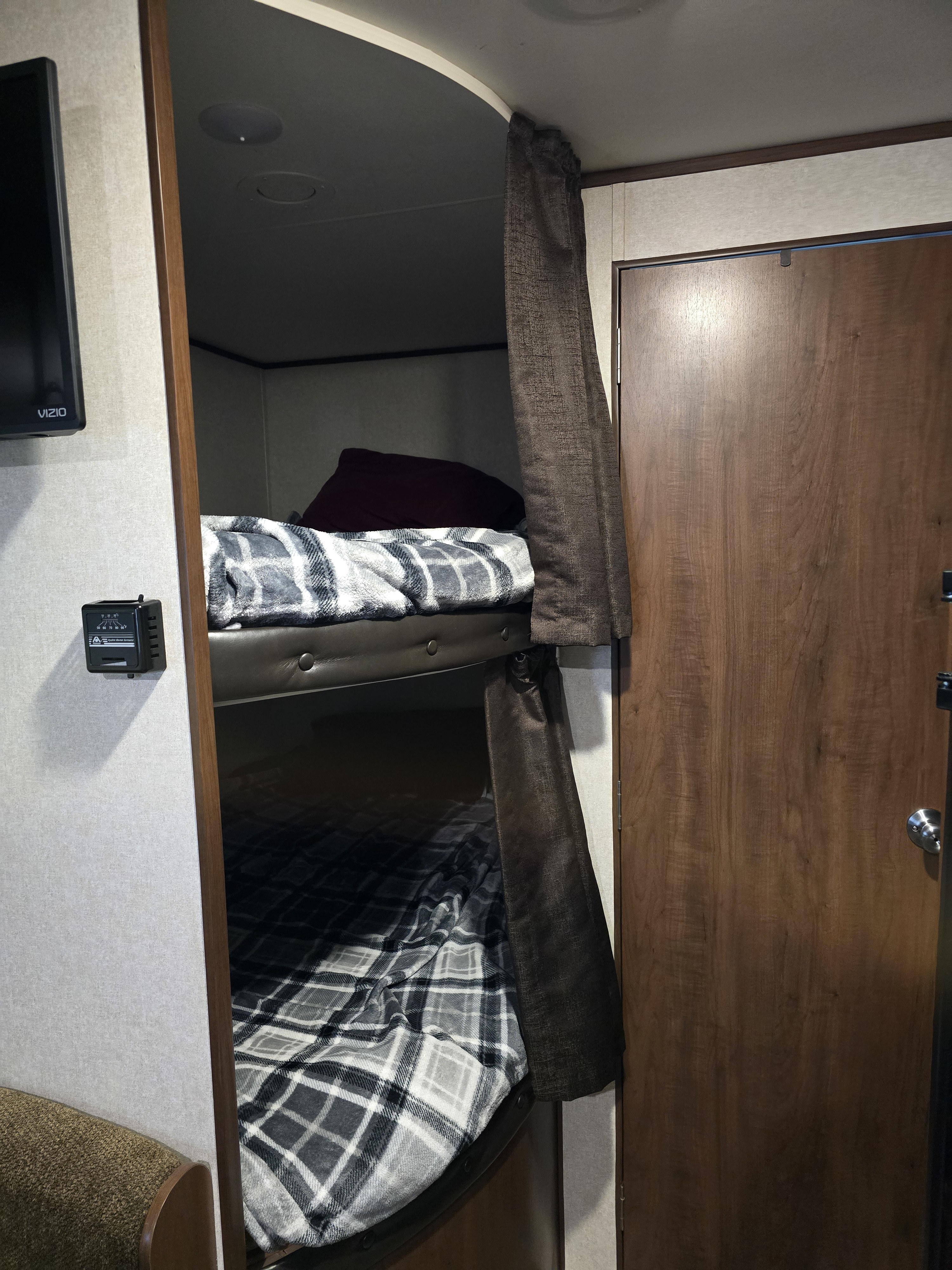 Cozy RV rental interior: bunk beds with plaid blankets and privacy curtain, alongside a door and wall-mounted TV.. Jayco Jay Flight SLX 2017