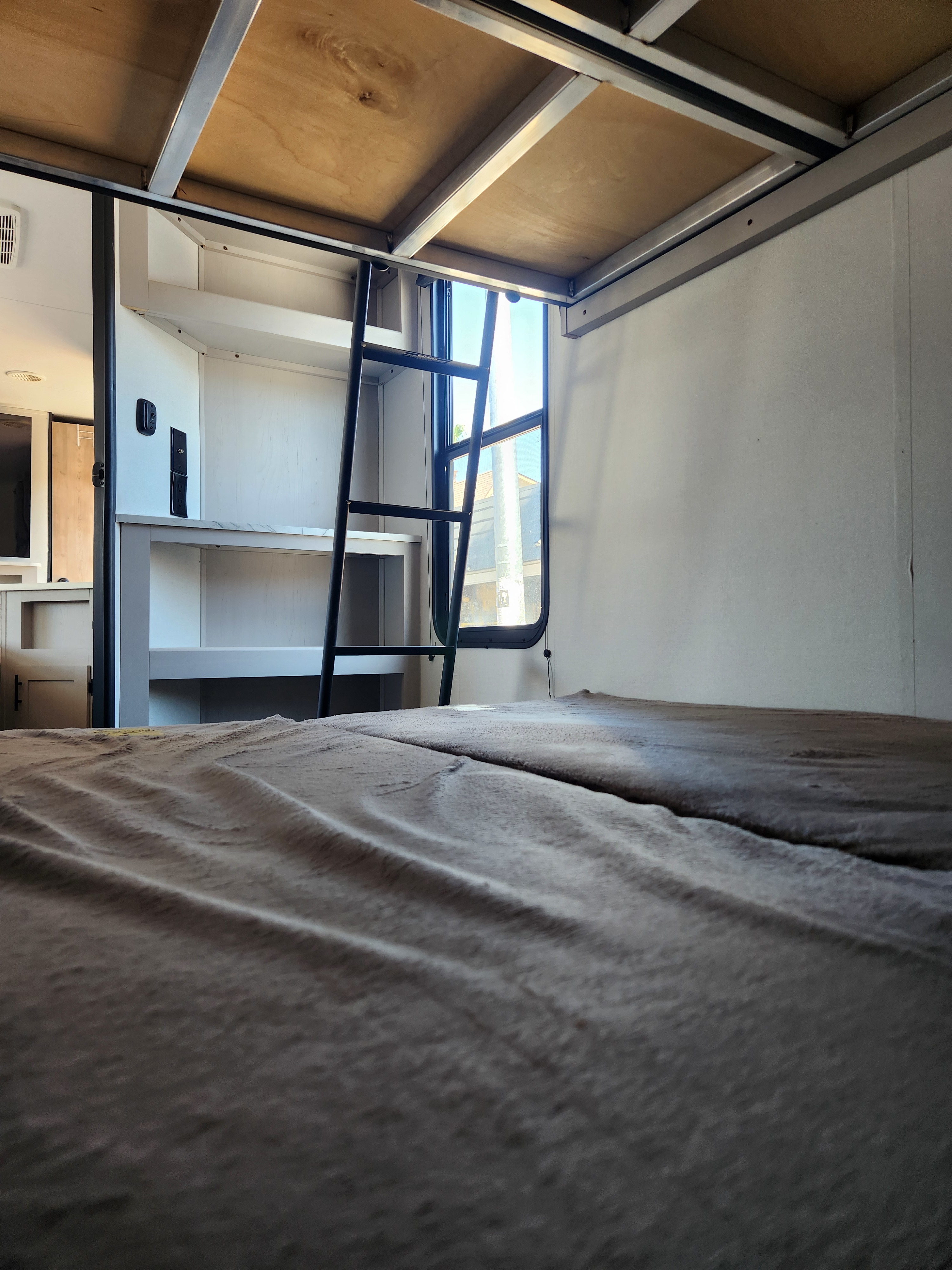 RV rental bunk bed setup: View from the lower bed, featuring a ladder, window, and built-in shelving.. Heartland RVs Prowler 2024