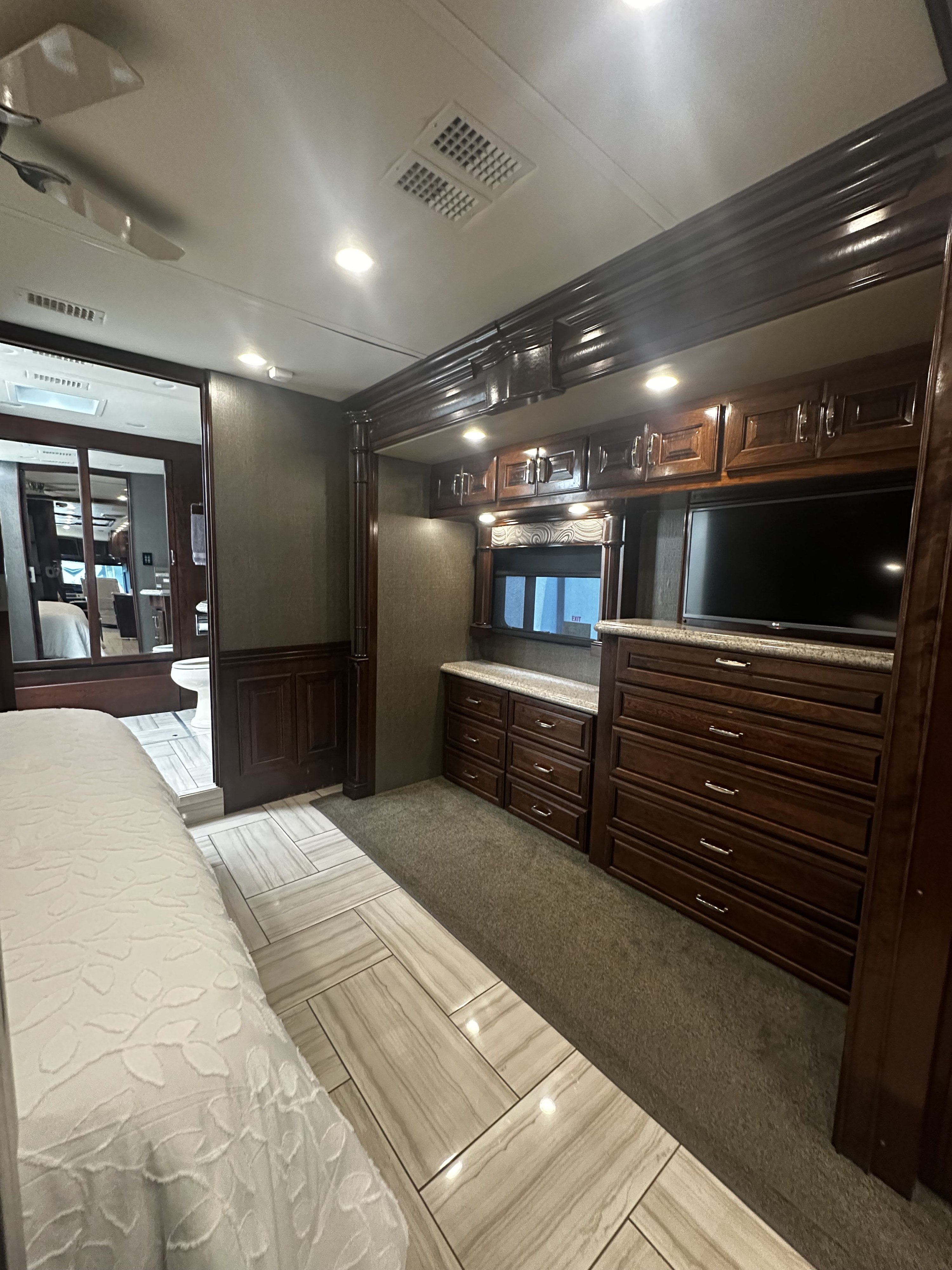 Explore this RV rental bedroom, featuring elegant dark wood cabinetry, integrated TV, and a comfy bed.. American Revolution American Revolution Motorhome 2017