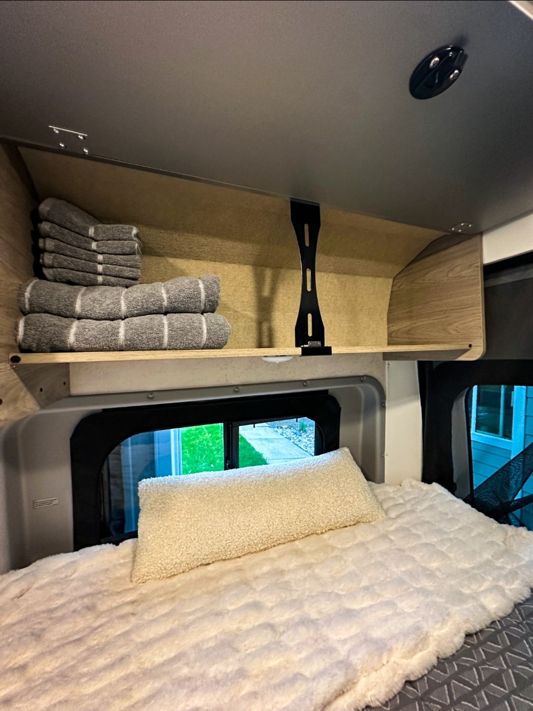 Explore this RV rental's cozy interior, featuring a soft bed and overhead storage with neatly folded towels.. Winnebago Solis 2022
