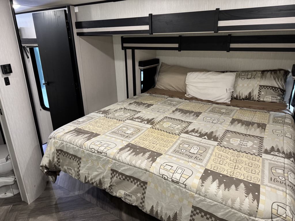 This rv rental features a cozy bedroom with camping-themed bedding, pillows, and overhead bunk beds, perfect for family adventures.. Heartland Cyclone 2022