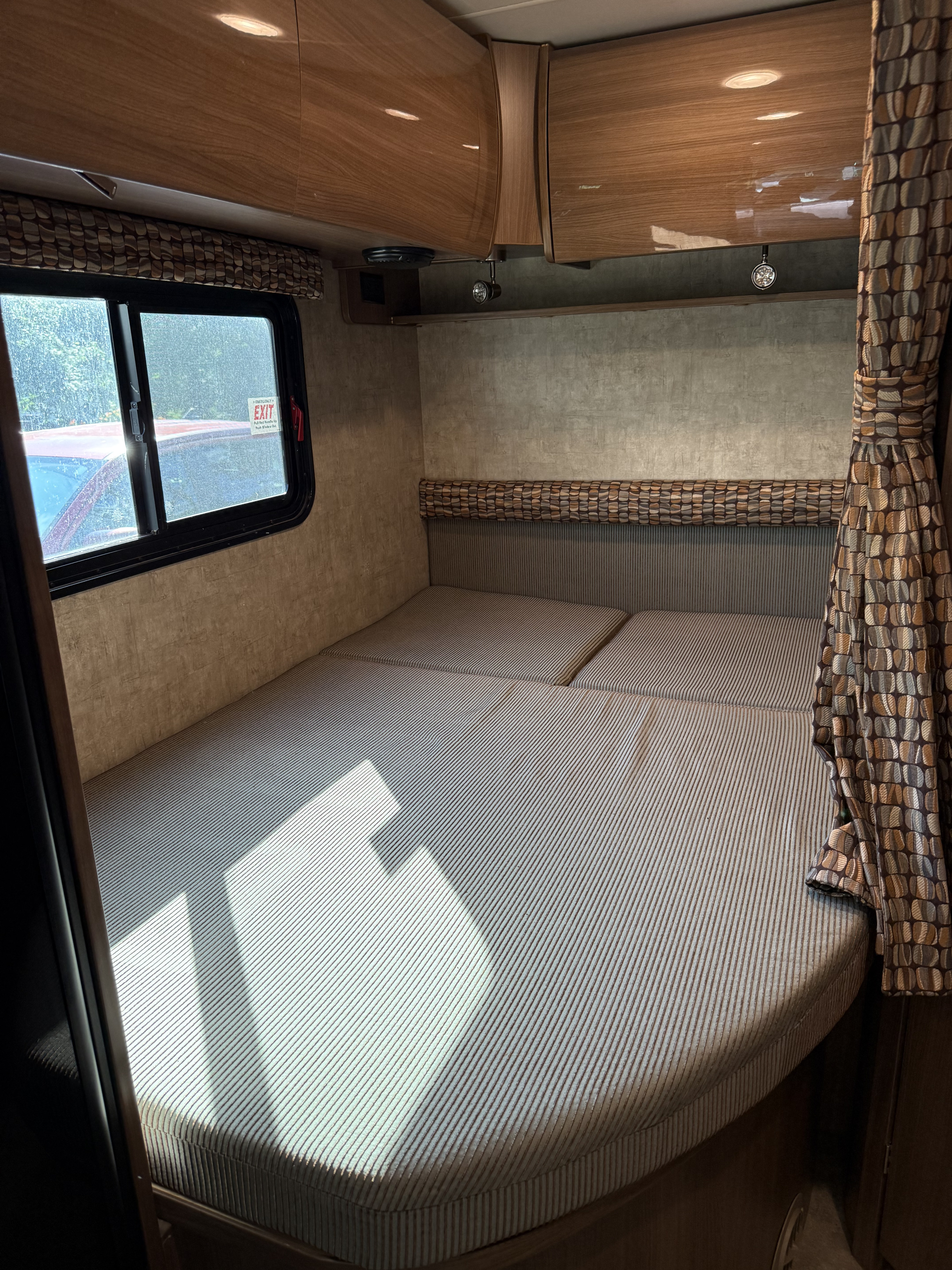 RV rental bedroom with striped cushions, window emergency exit, and overhead storage. Ready for your adventure.. Itasca Viva 2015