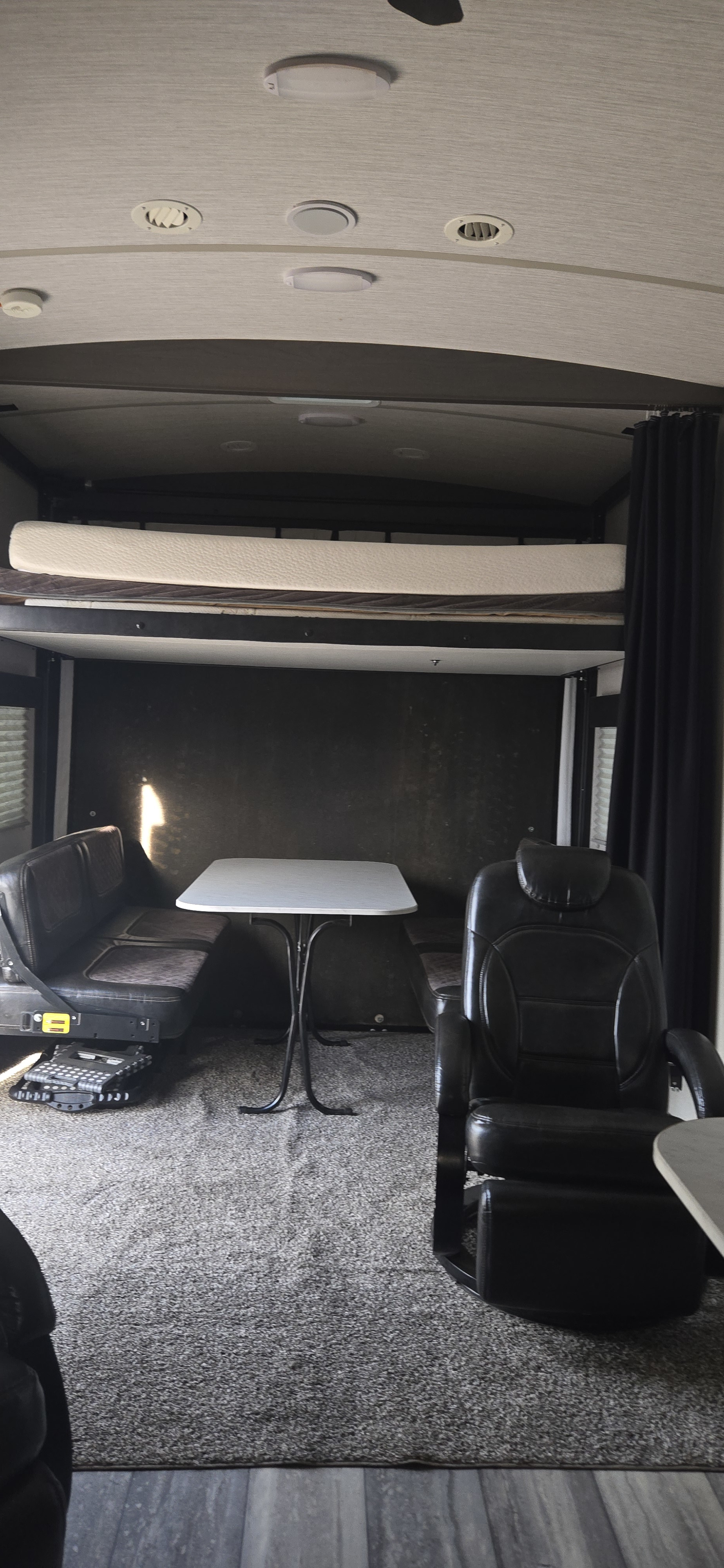 Spacious RV rental interior featuring a convertible living/dining area with benches, a recliner, and an elevated bunk bed. Carpeted floor.. Heartland Fuel 305 2020