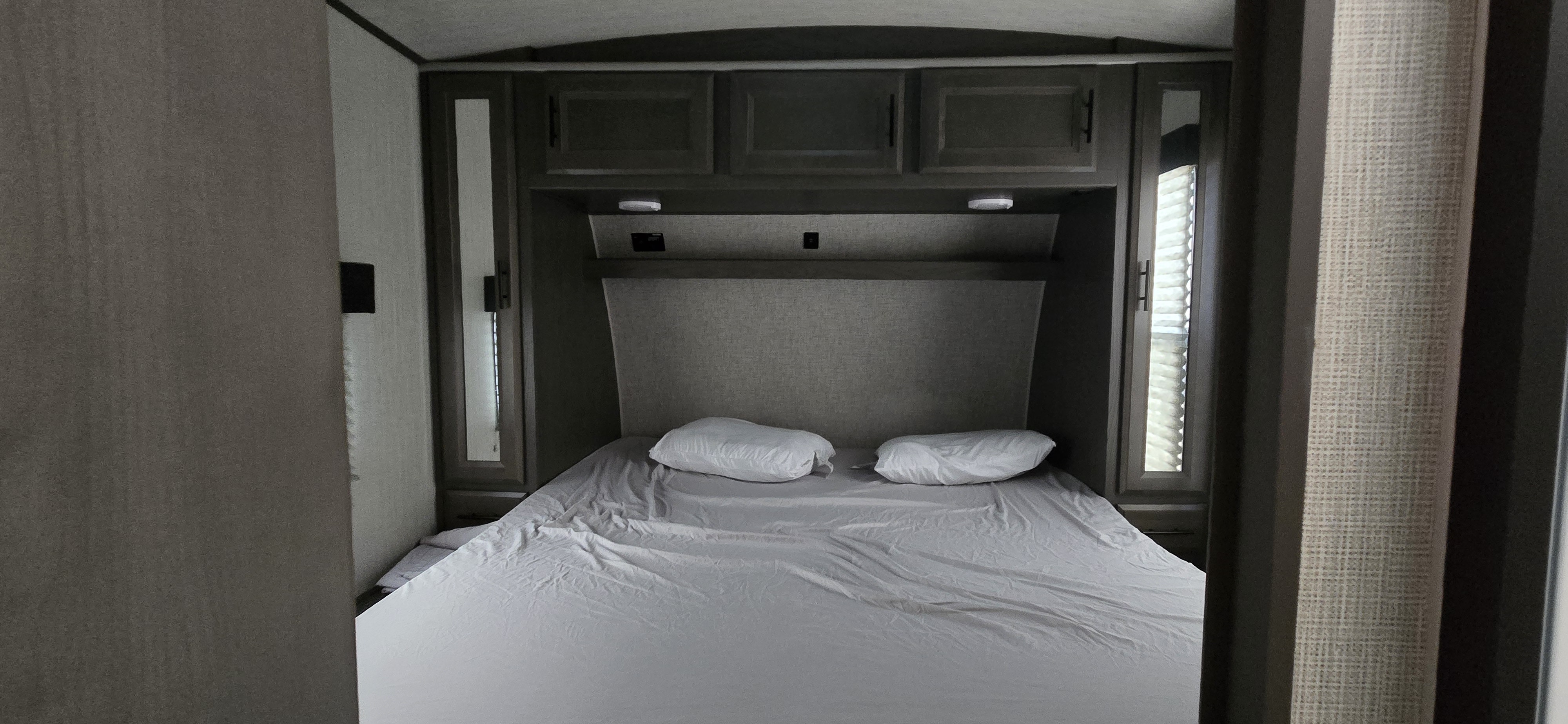 Cozy RV rental bedroom with queen bed, overhead storage, and mirrored side wardrobes, offering a compact sleeping area.. Heartland Fuel 305 2020