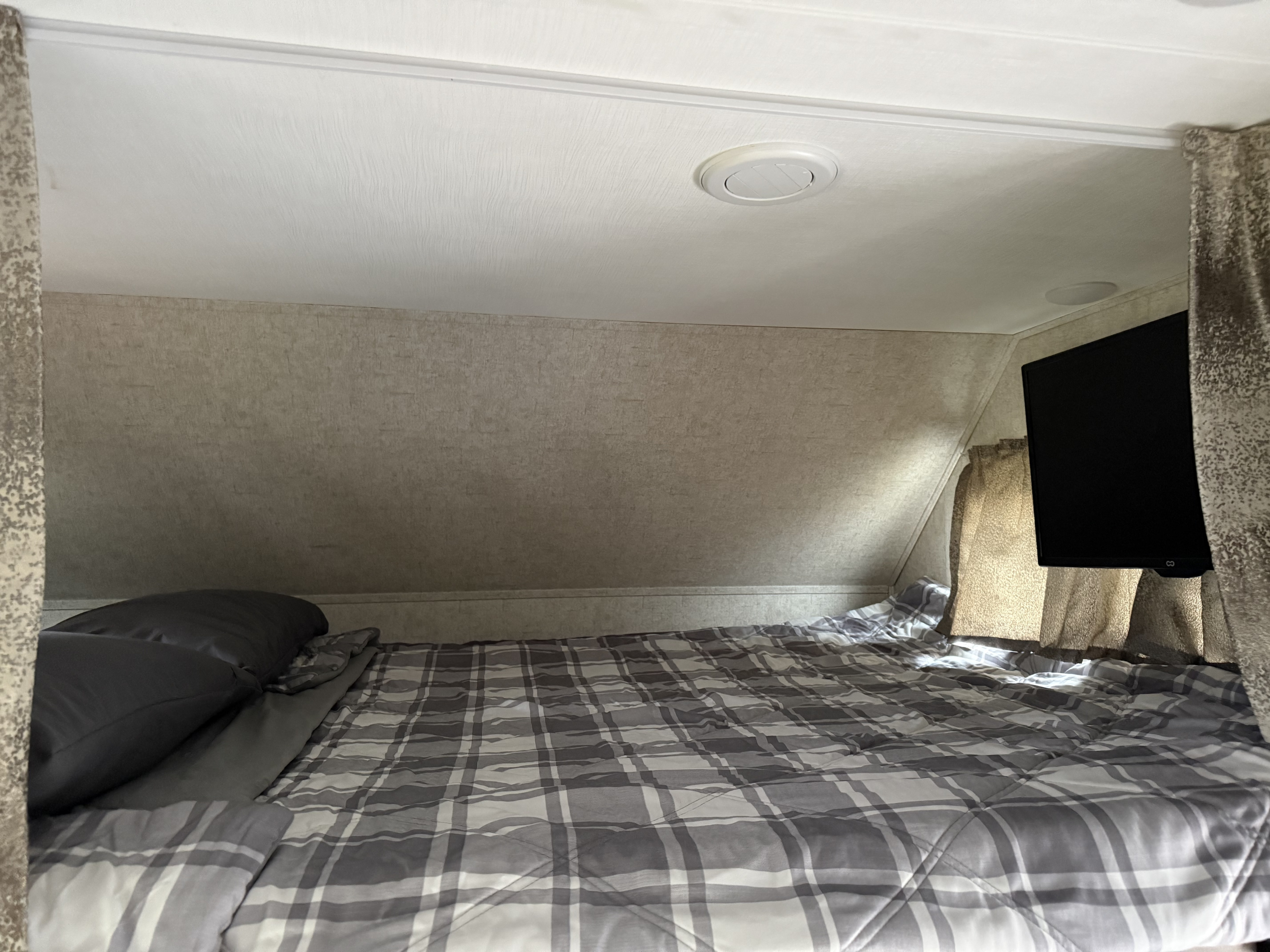 An RV rental bunk bed area with a gray plaid comforter, dark pillows, and a mounted TV for comfortable sleeping.. Forester Forester Motorhome 2020