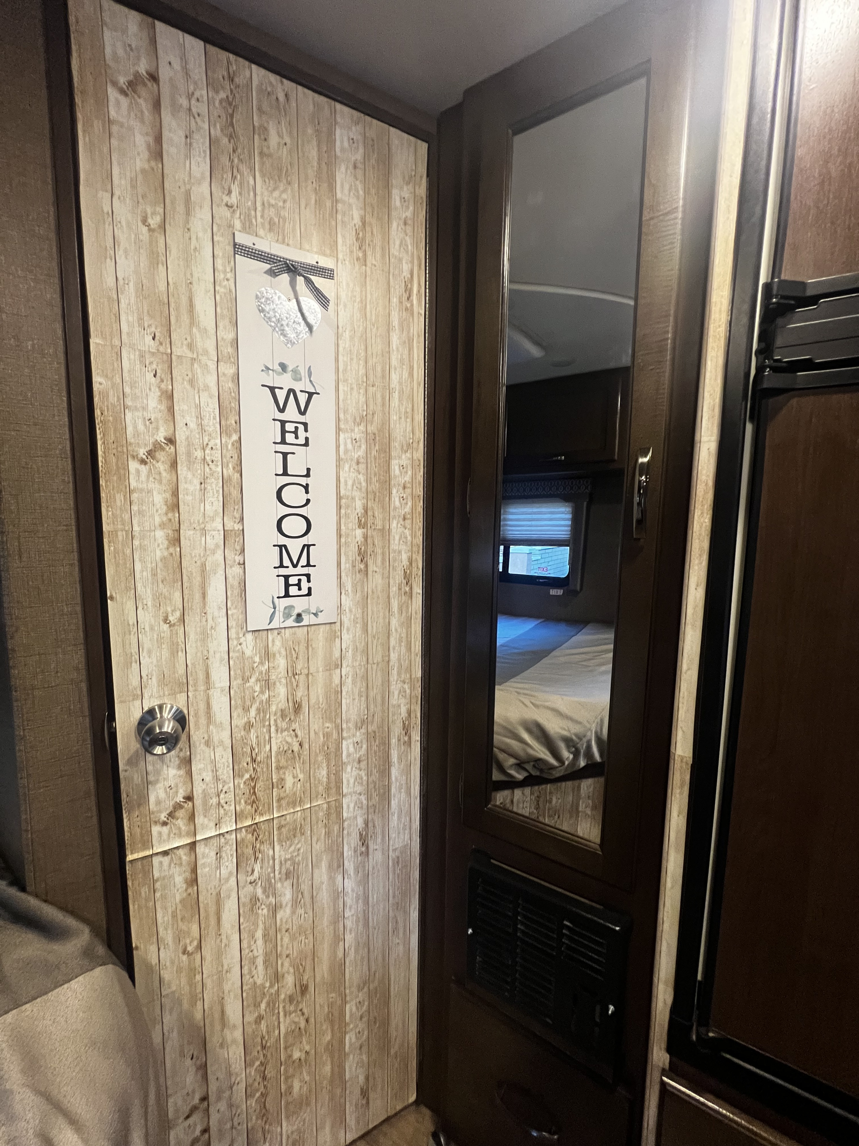 Cozy RV rental interior featuring a wood-look door with a welcome sign and mirrored reflection of the bedroom space.. Thor Freedom Elite 2018