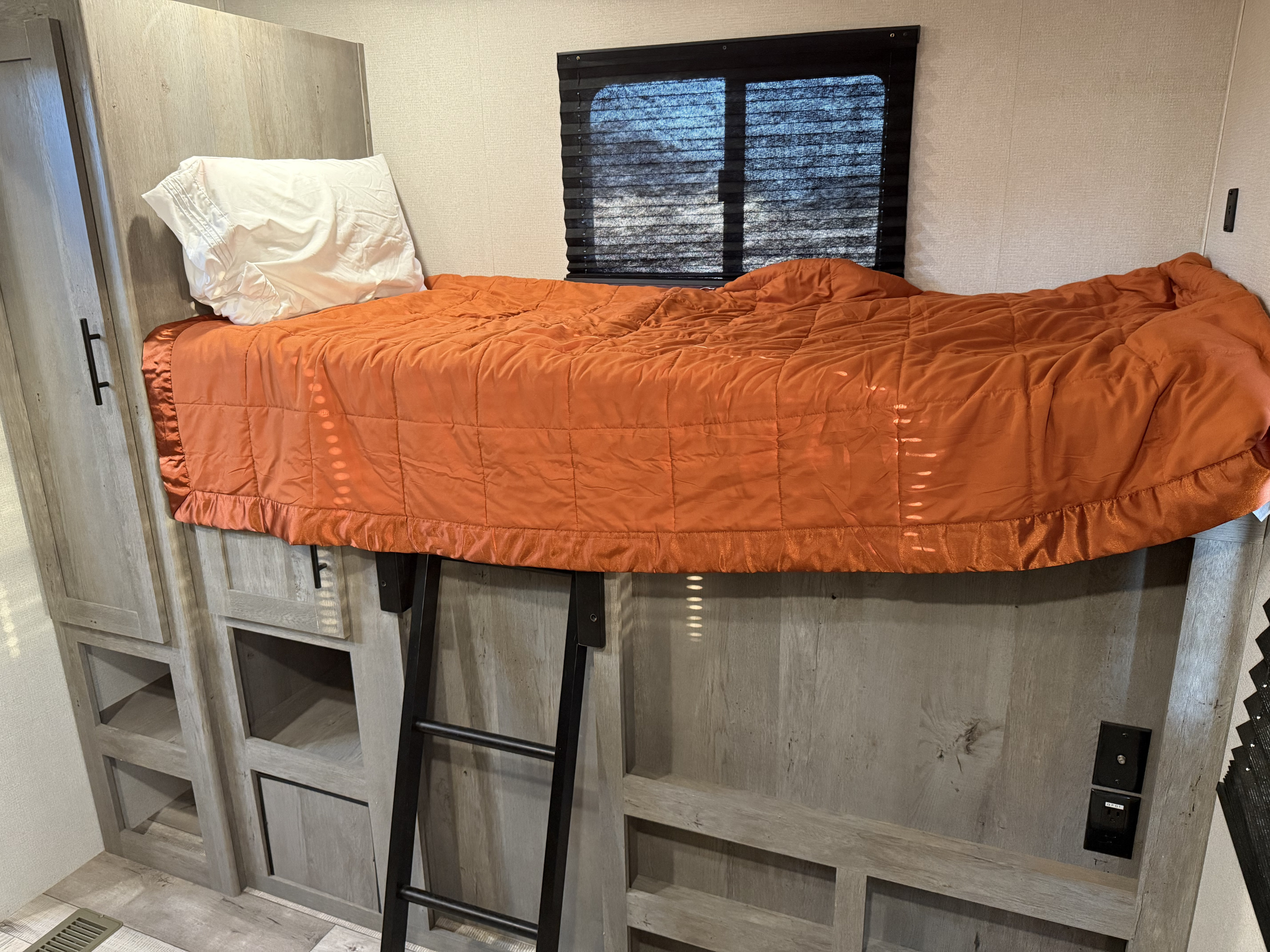 RV rental: a cozy bunk bed with an orange comforter, white pillow, ladder, and built-in storage below.. Keystone RV Springdale 2021