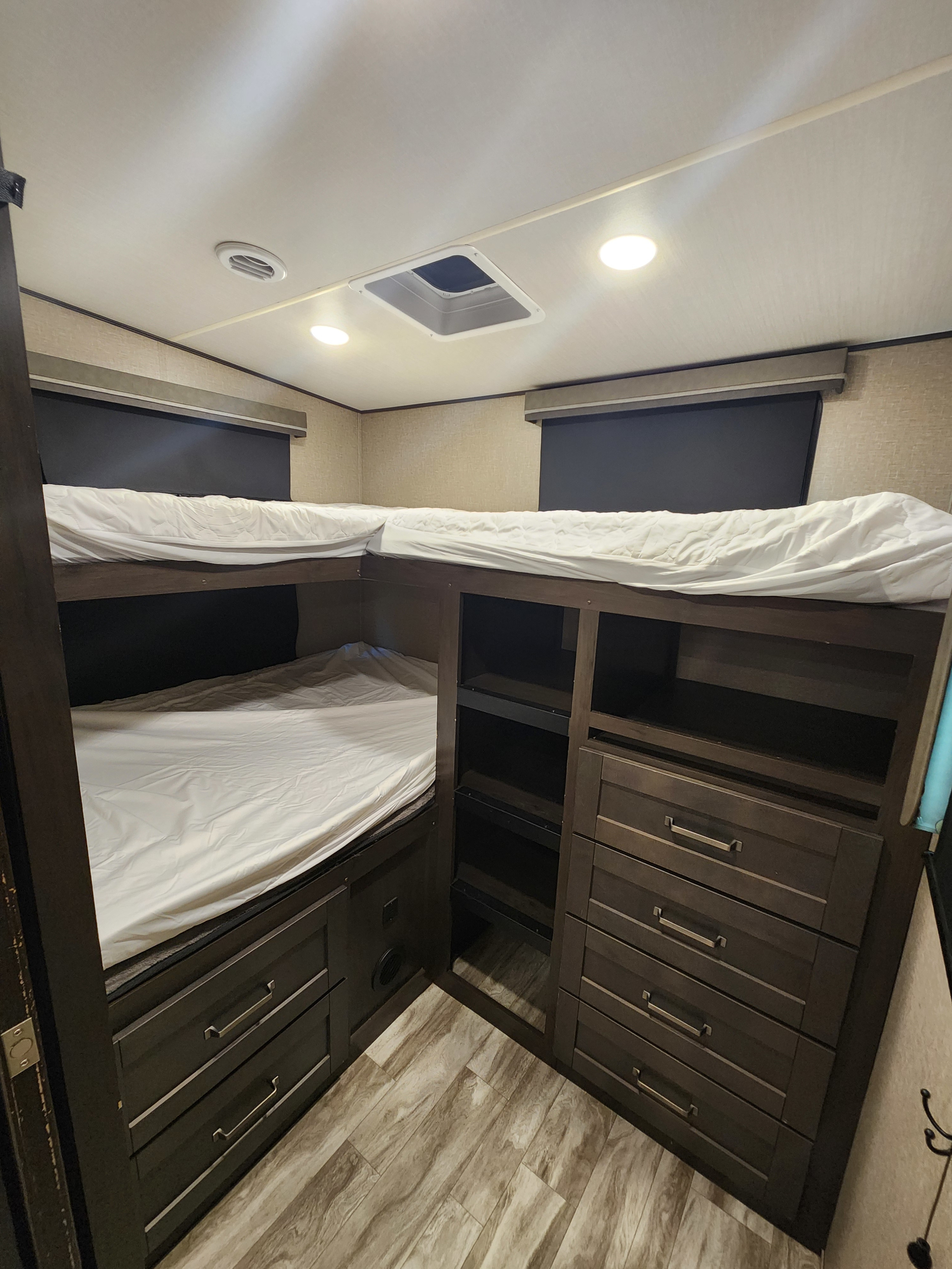 Spacious RV rental bunk room features cozy bunk beds with white bedding, dark wood storage, and bright lighting.. Grand Design Reflection 2020