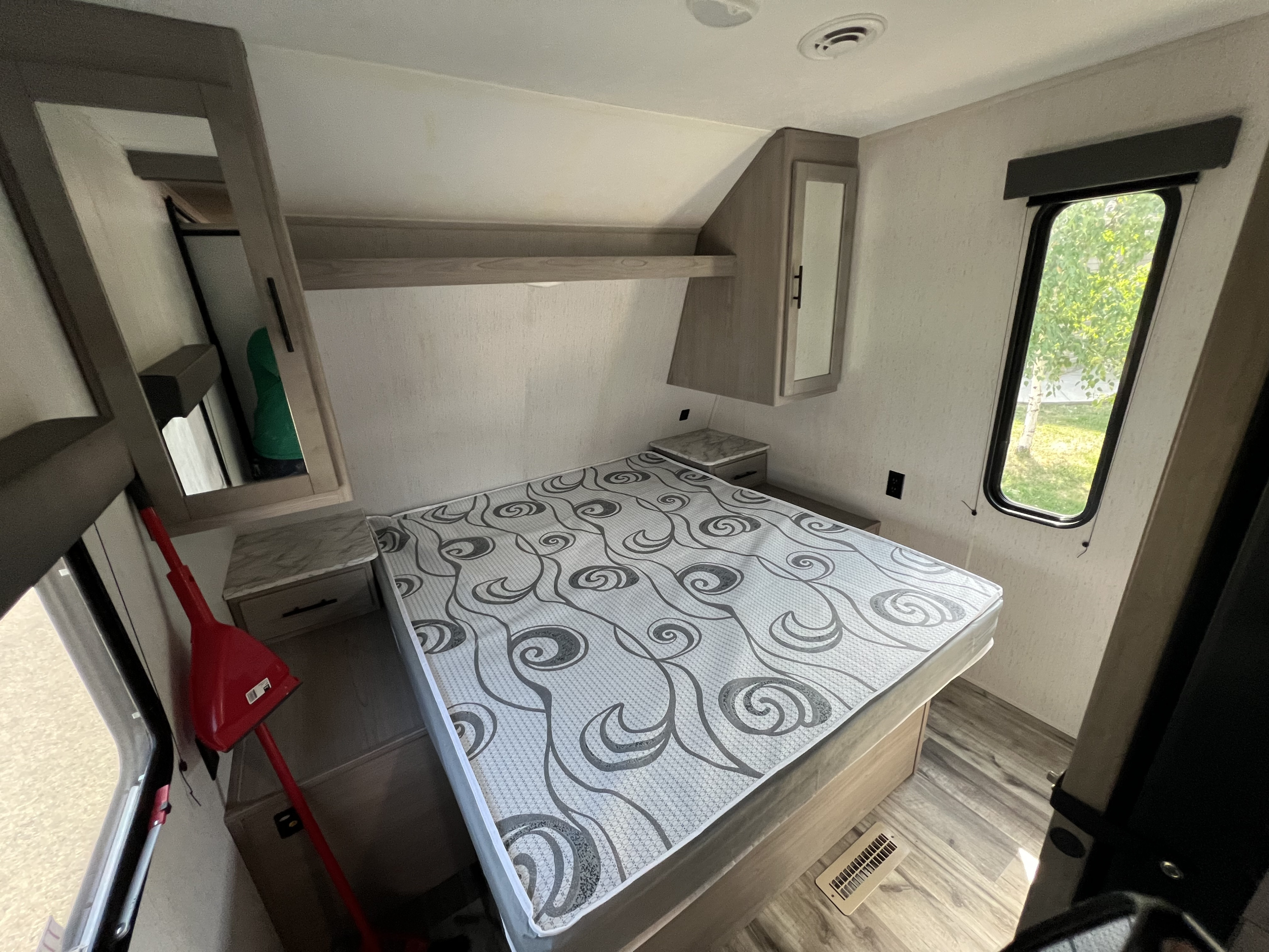 Cozy RV rental bedroom interior with patterned mattress, overhead storage, and a window, ideal for travel.. Dutchmen Coleman Lantern 2022