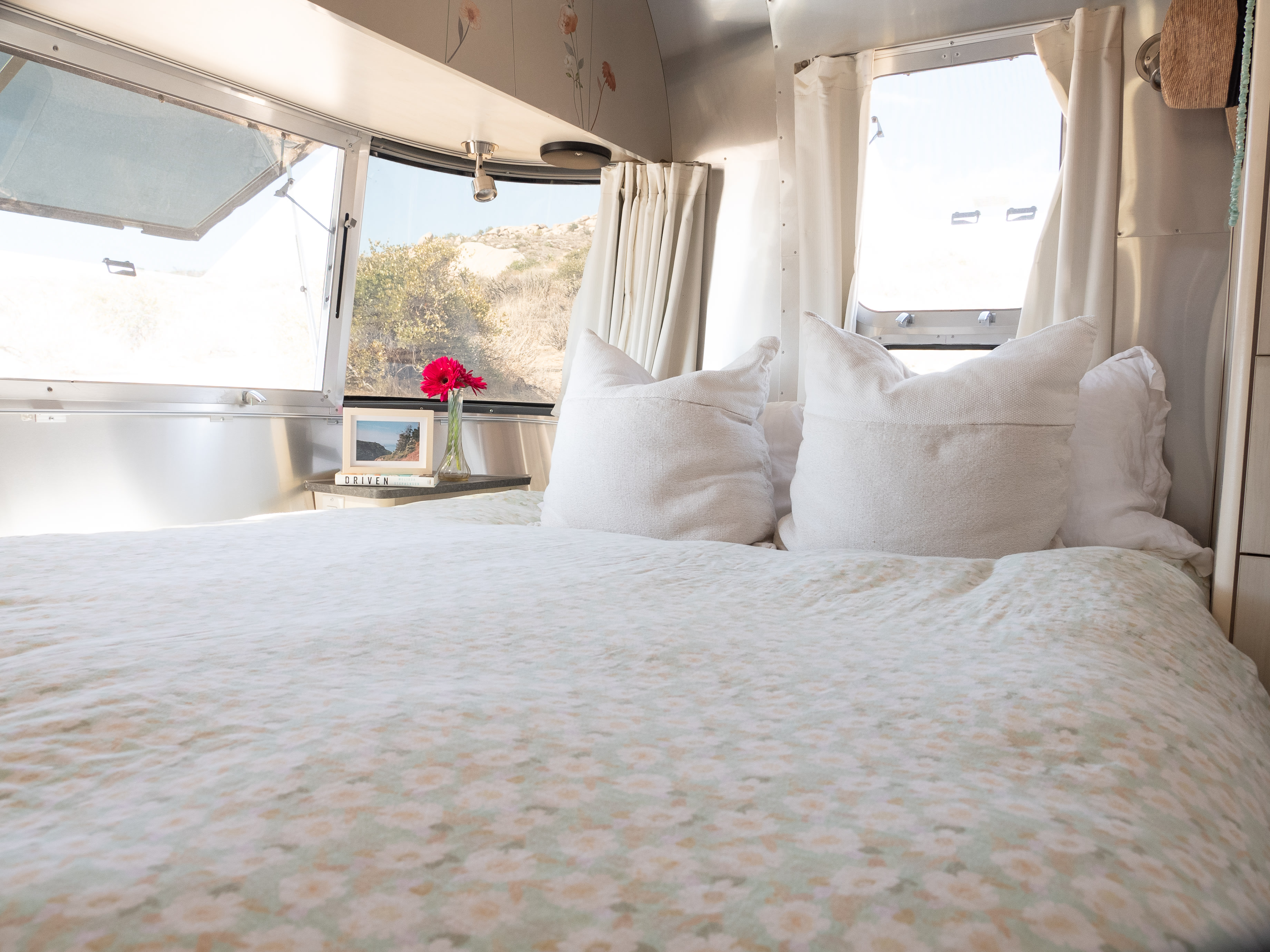 Cozy RV rental bedroom with floral bedding, white pillows, and scenic desert views through large windows.. Airstream Flying Cloud 2022