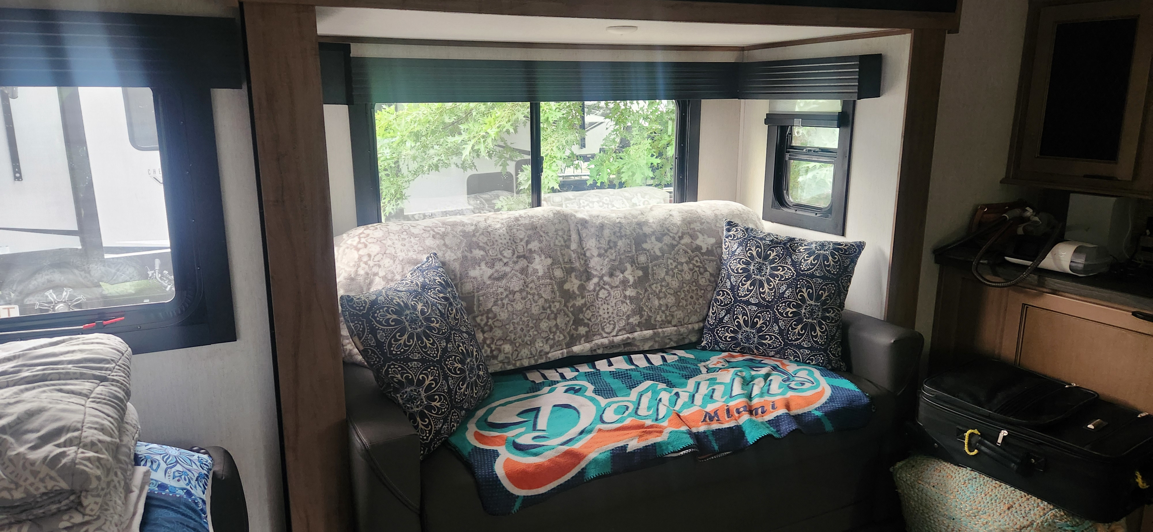 Cozy RV rental interior with sofa, decorative pillows, and Miami Dolphins blanket. Windows show trees outside.. Forest River Sabre 37FLH 2024