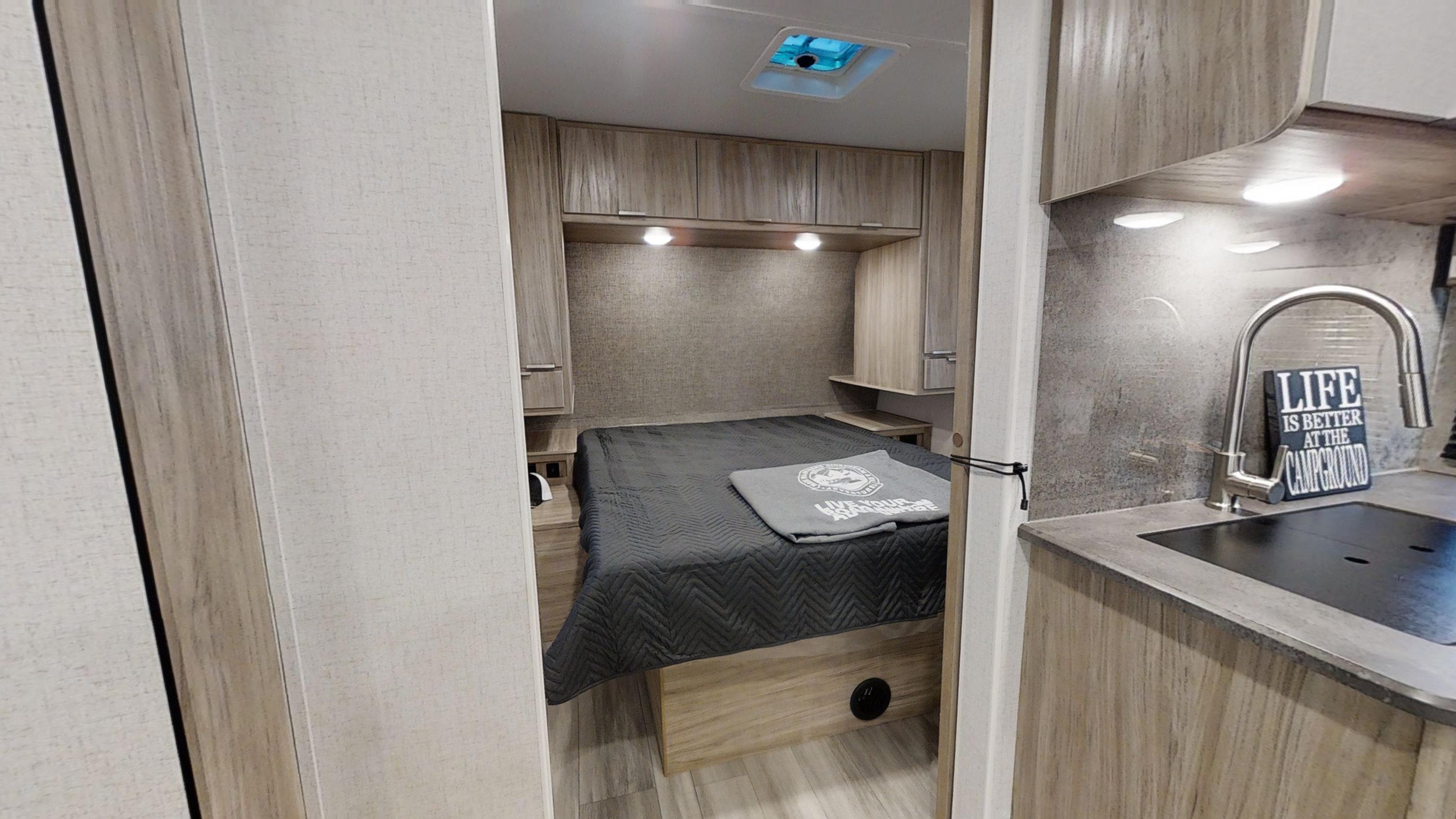 This inviting RV rental interior showcases a cozy bedroom with overhead storage, leading to a compact kitchenette. Perfect for travel!. Winnebago Minnie 2301BHS 2021