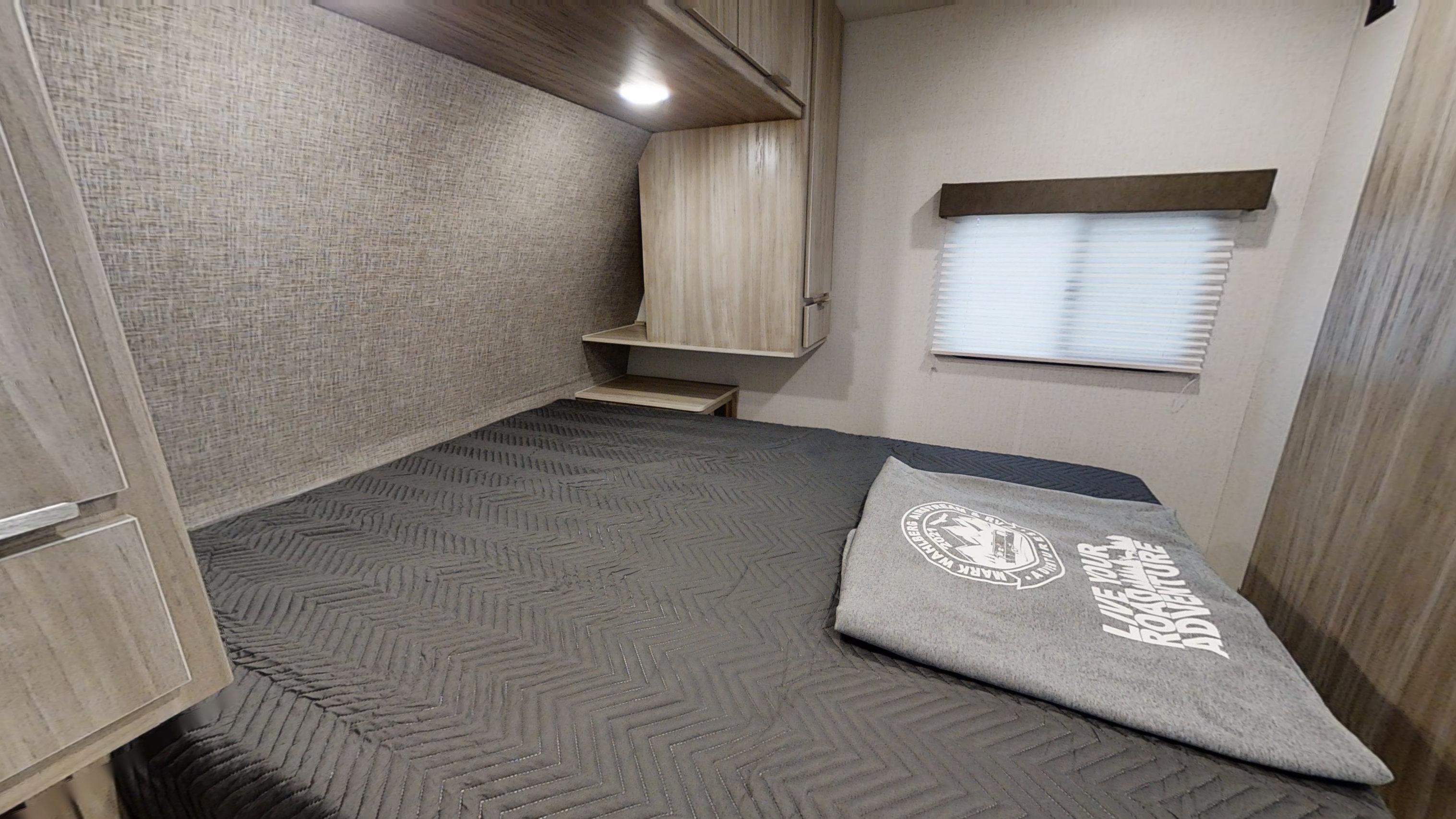 Comfortable RV rental bedroom with textured walls, a modern gray bedspread, overhead storage, and a window blind.. Winnebago Minnie 2301BHS 2021