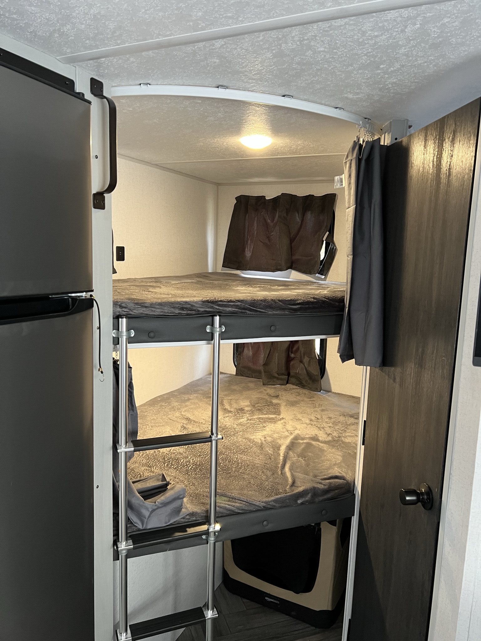 Inside this RV rental: functional bunk beds with a ladder, an adjacent refrigerator, and a pet crate below.. Forest River Wildwood 2022