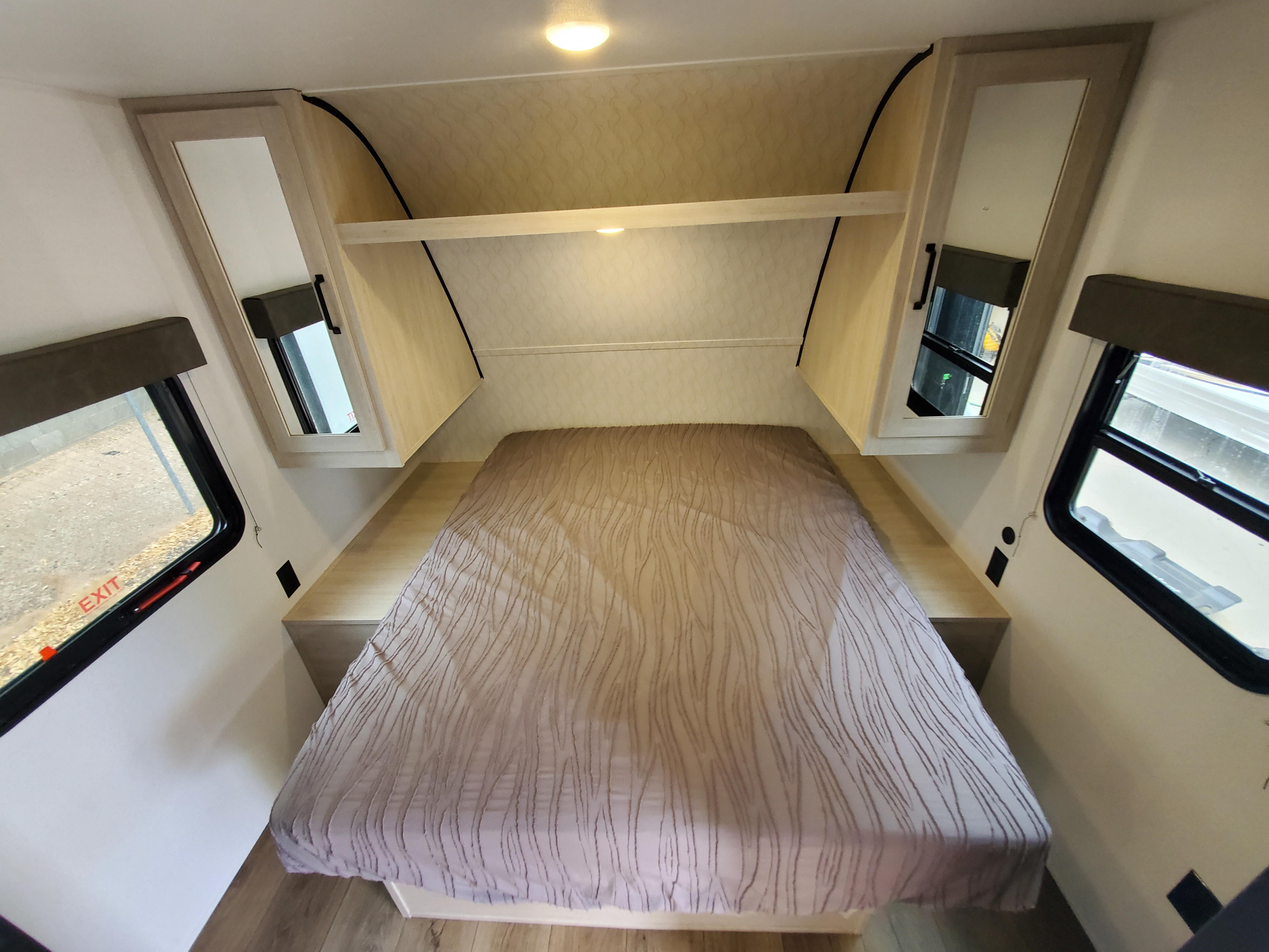 Cozy RV rental bedroom featuring a comfortable bed, mirrored cabinets, overhead shelf with lighting, and windows on both sides.. forest river Puma 2025